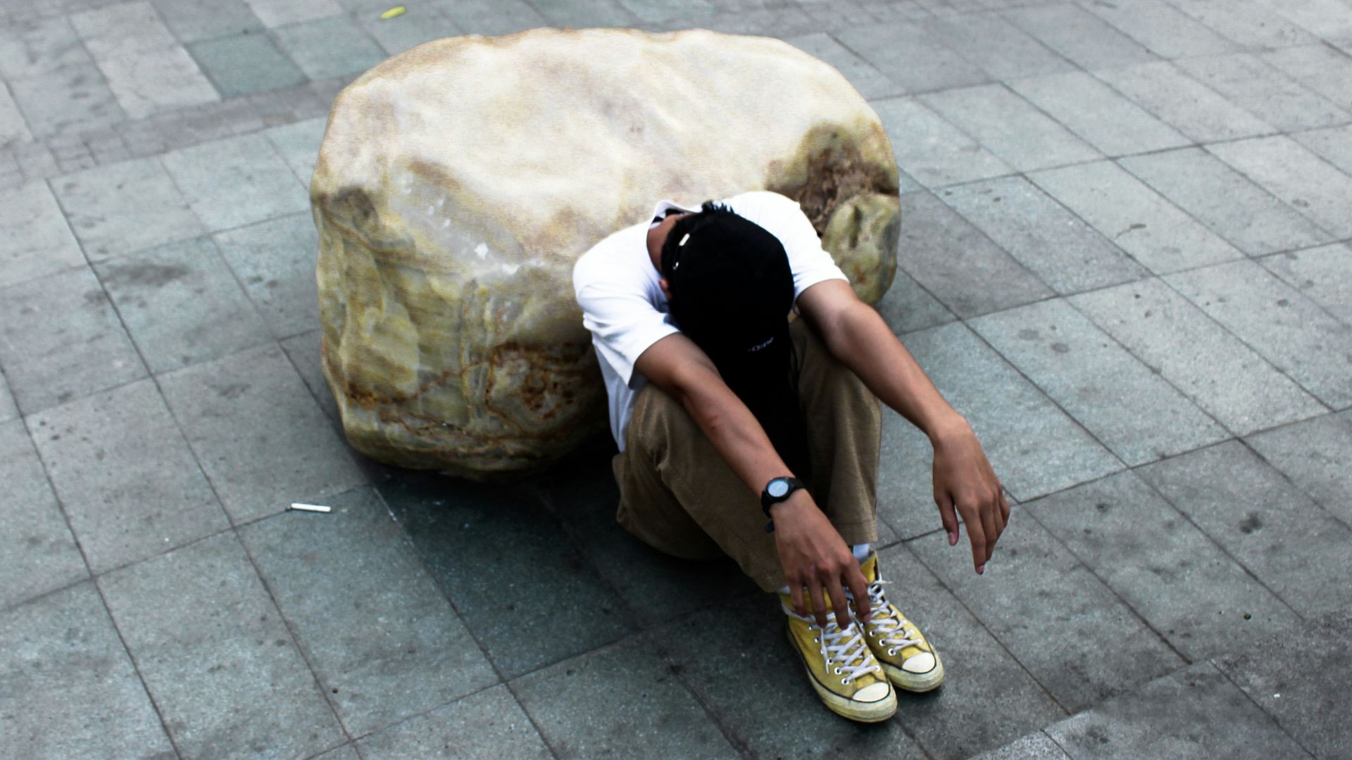person looking down while siting on concrete pathway during daytime