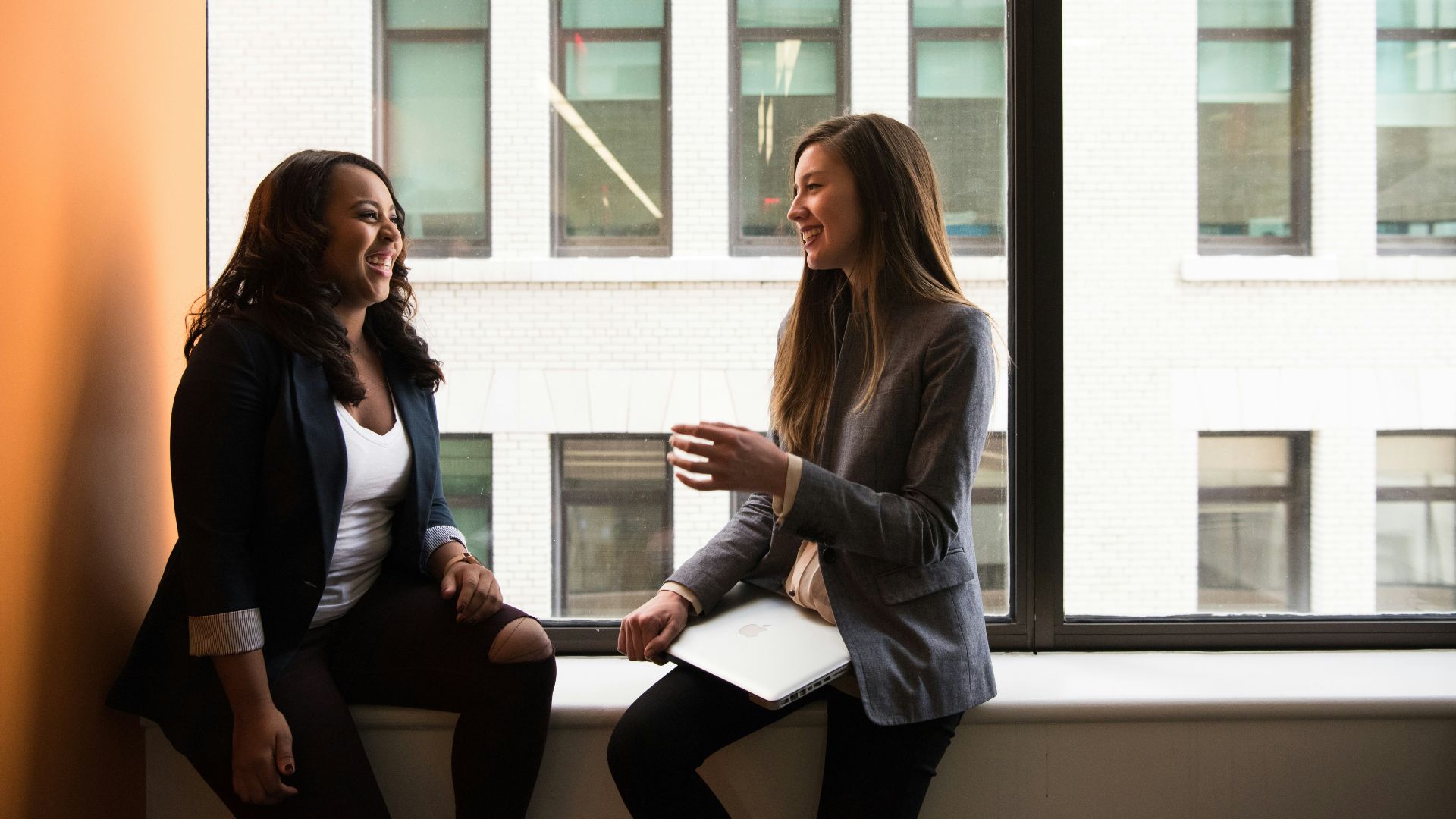 two woman sitting by the window laughing