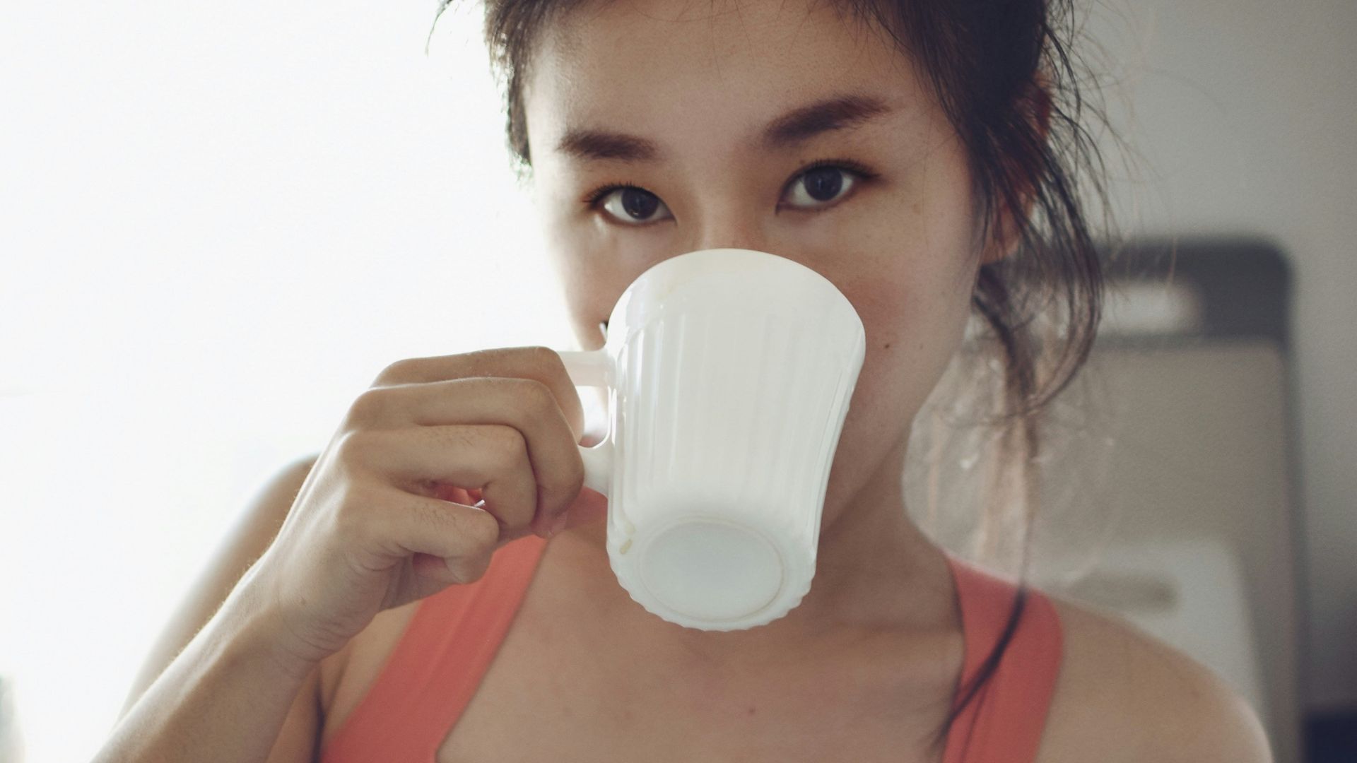 woman in red sports bra drinking from white ceramic mug