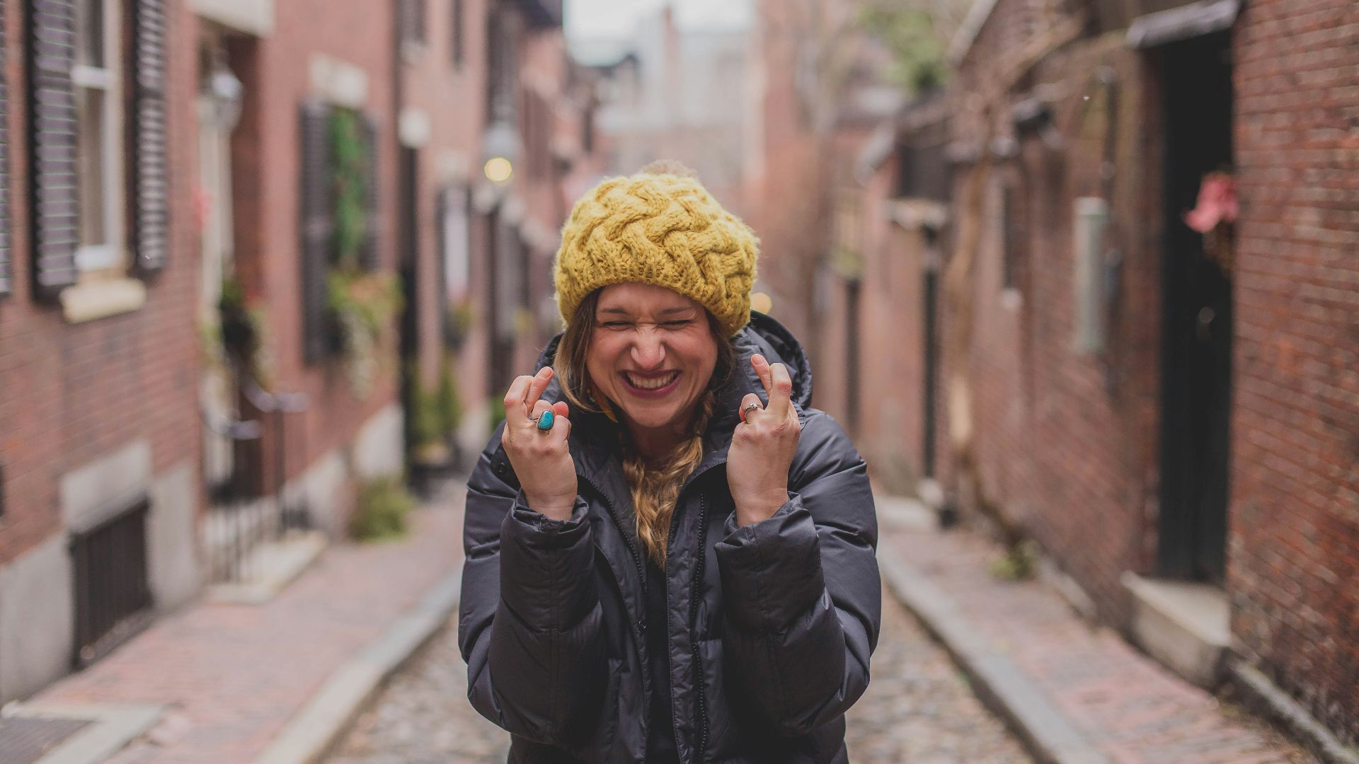 woman in black jacket and yellow knit cap standing on sidewalk during daytime