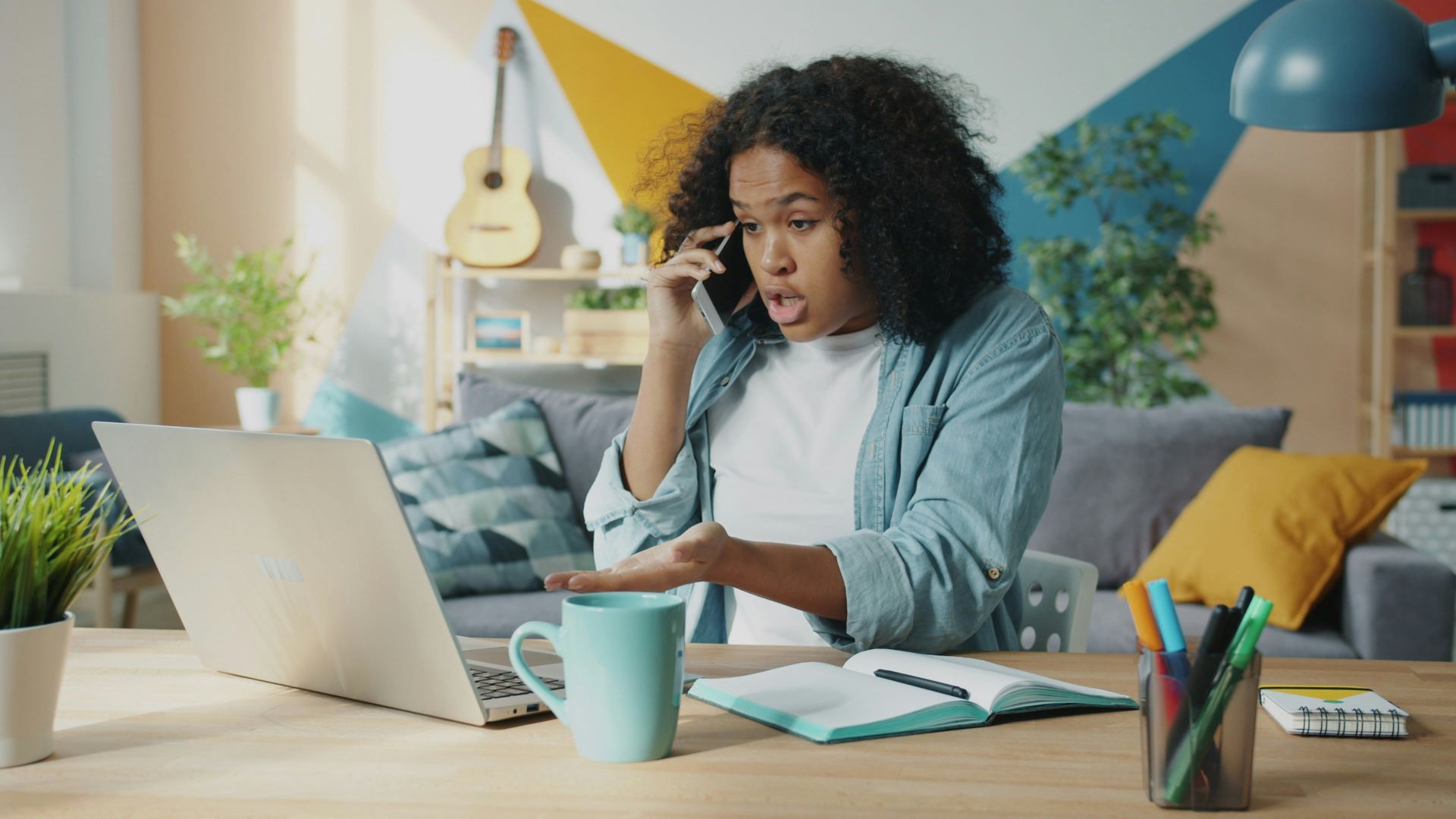 Young woman talking on phone at laptop desk.