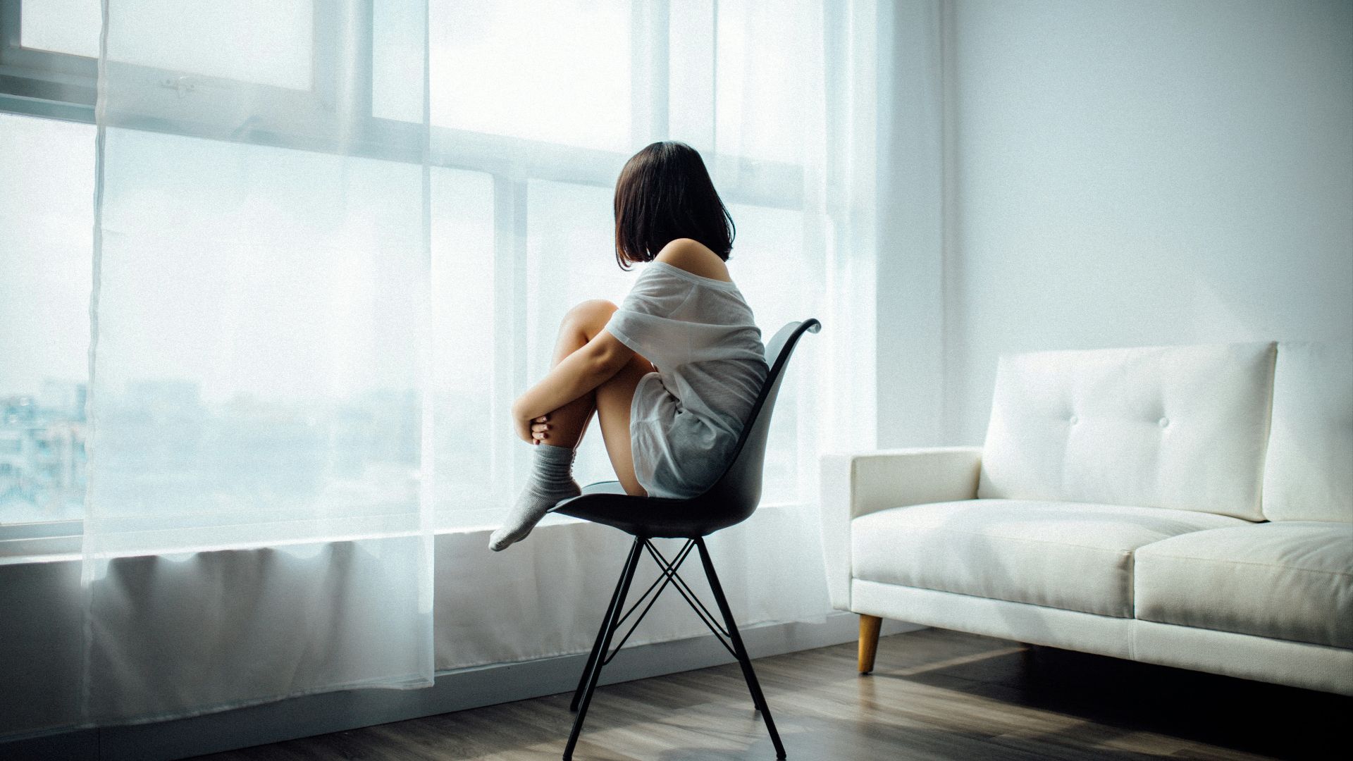 woman sitting on black chair in front of glass-panel window with white curtains
