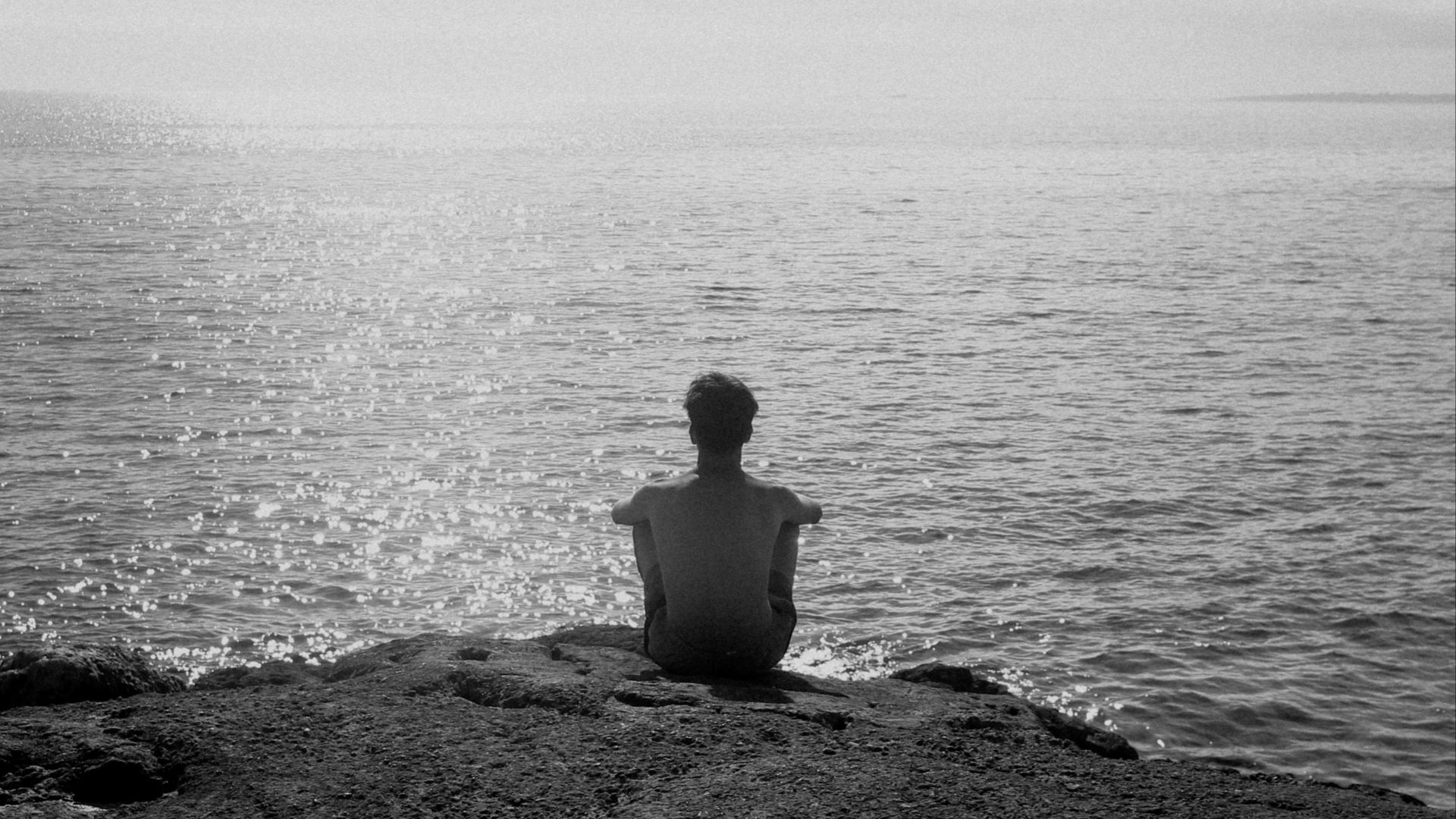A person sitting on a rock looking out at the ocean