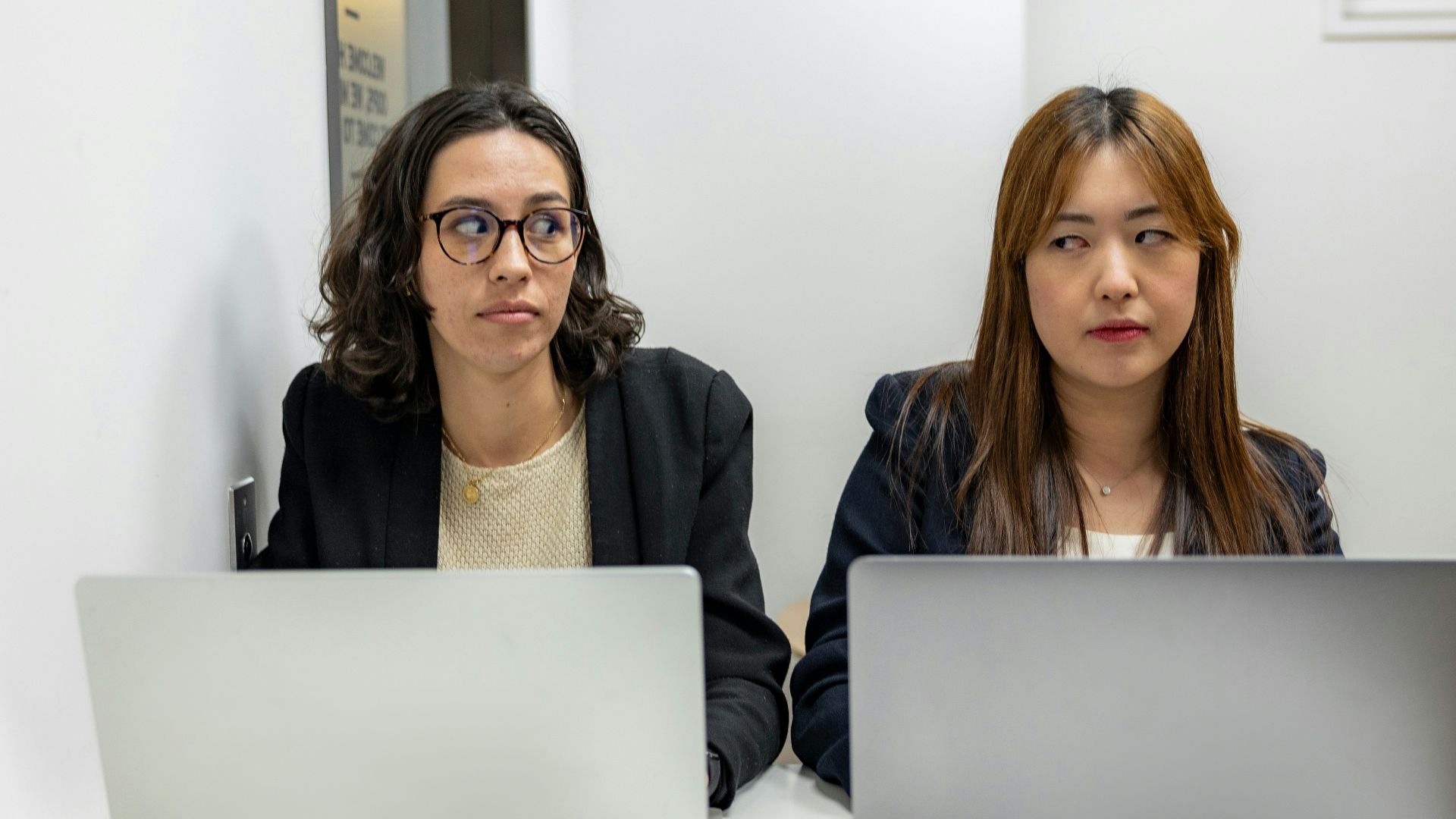 two women sitting at a table with laptops