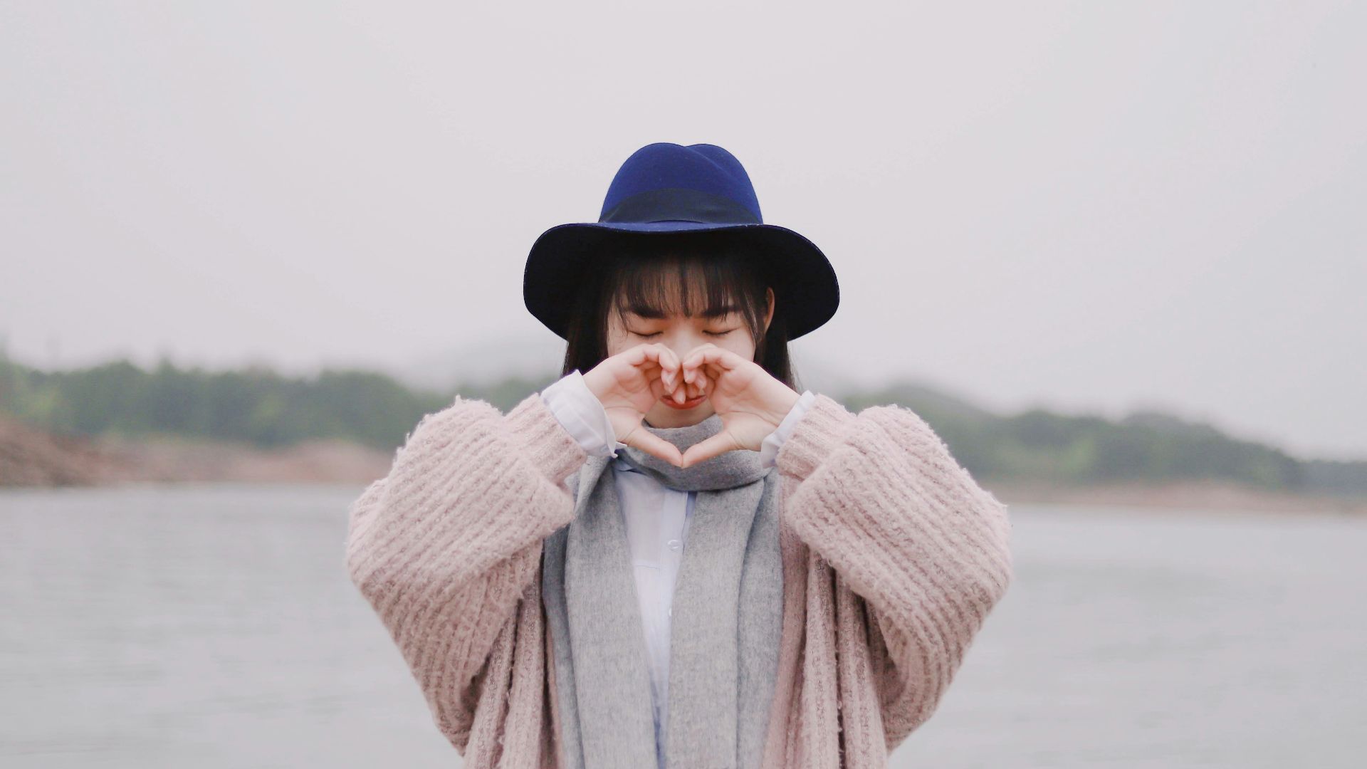 woman forming heart by hand near water