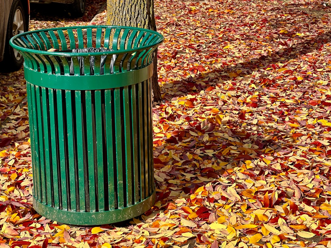 a green trash can sitting next to a tree