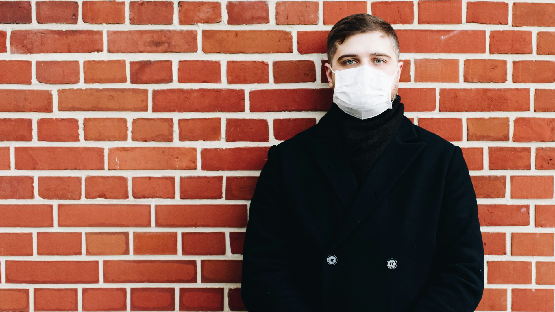 man in black coat standing beside brown brick wall