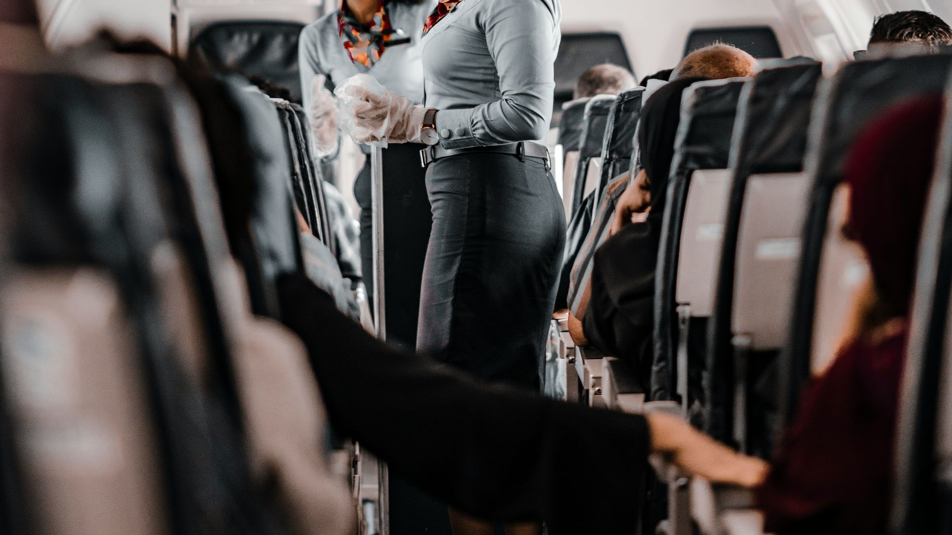 air hostess wearing a facemask standing in the aisle of an aeroplane