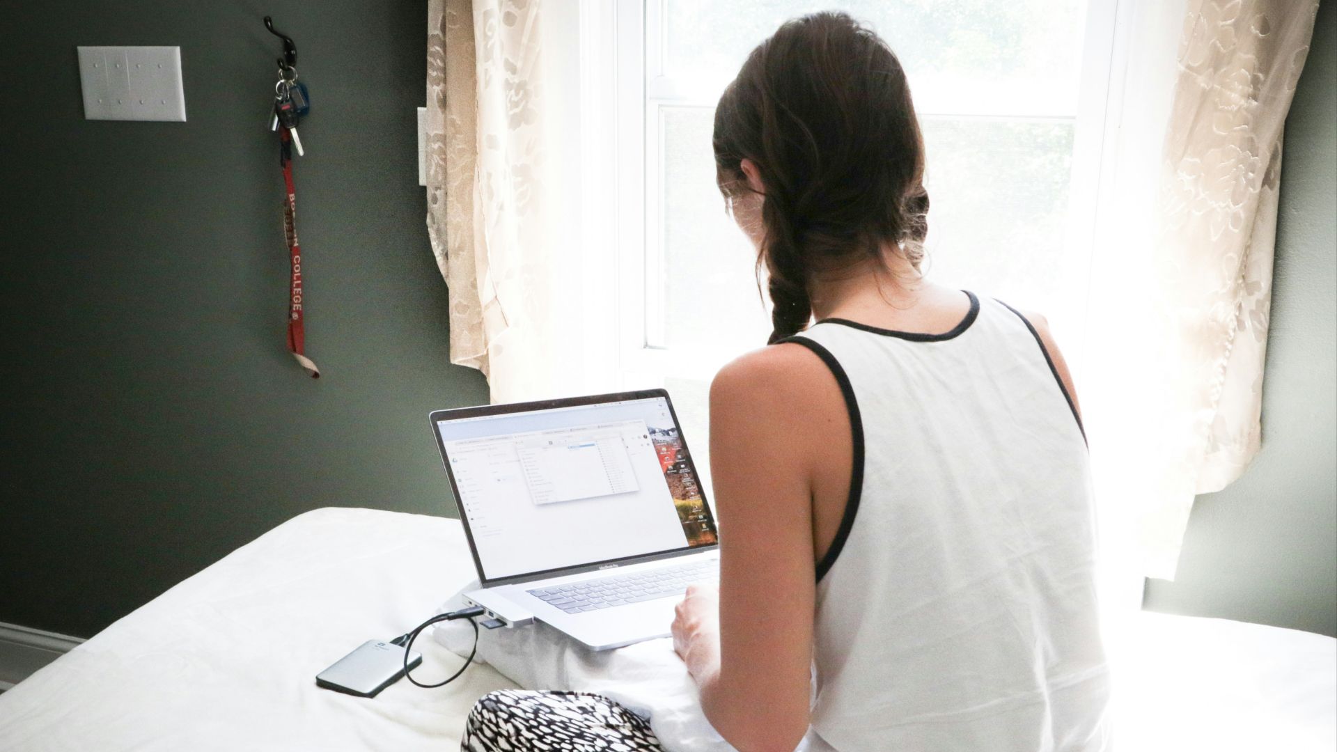 woman in white tank top sitting on bed in front of laptop computer