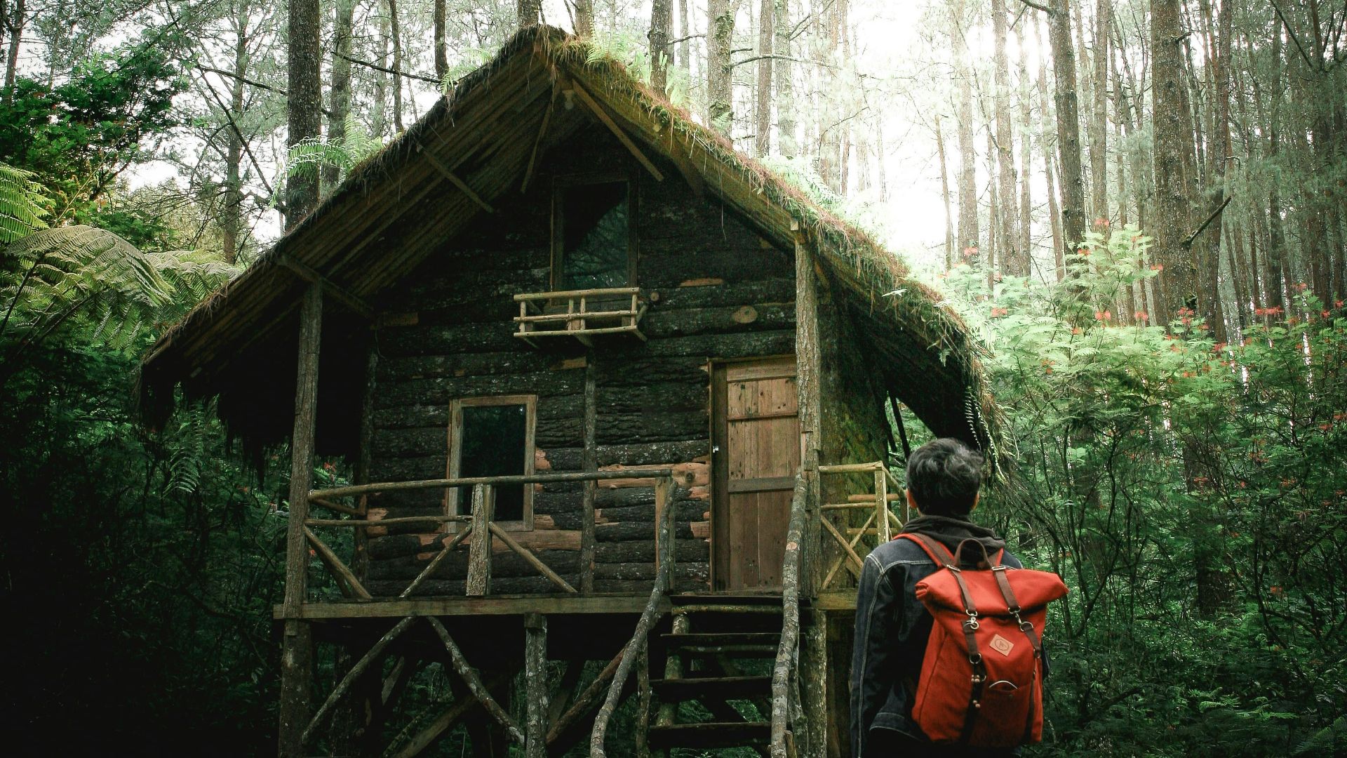 man with backpack beside a wooden house at the forest