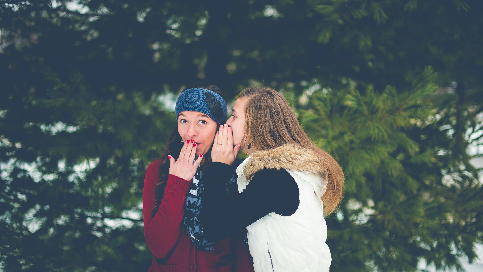 woman whispering on woman's ear while hands on lips
