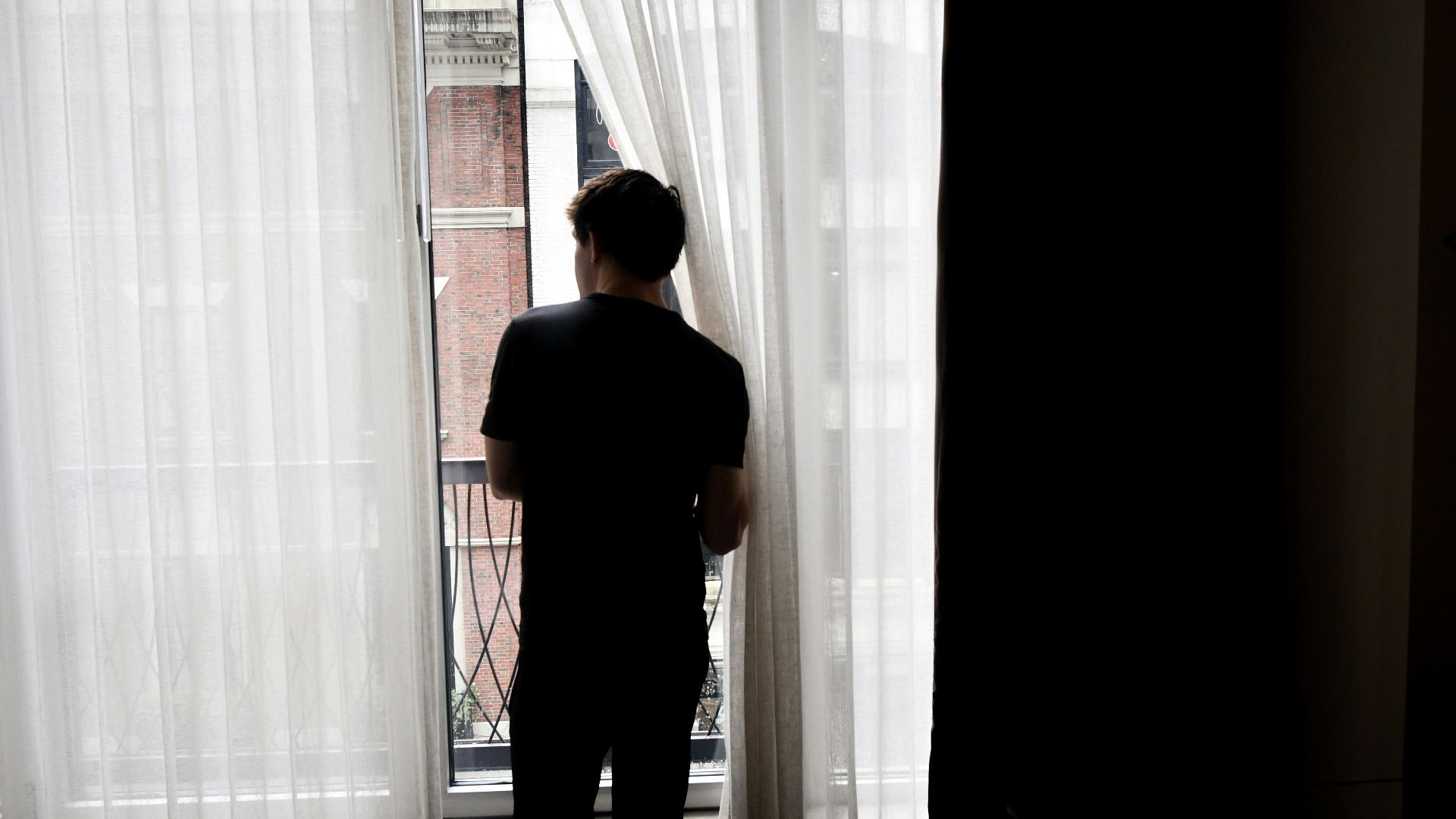 man in black crew neck t-shirt standing near white window curtain