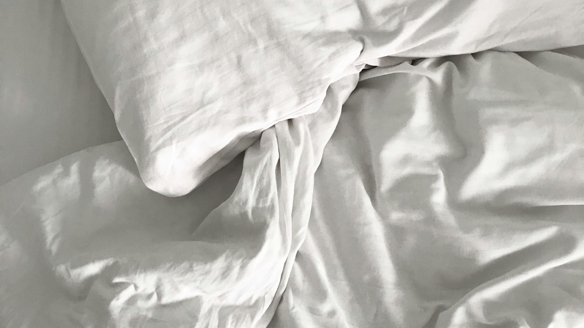 an unmade bed with white sheets and pillows