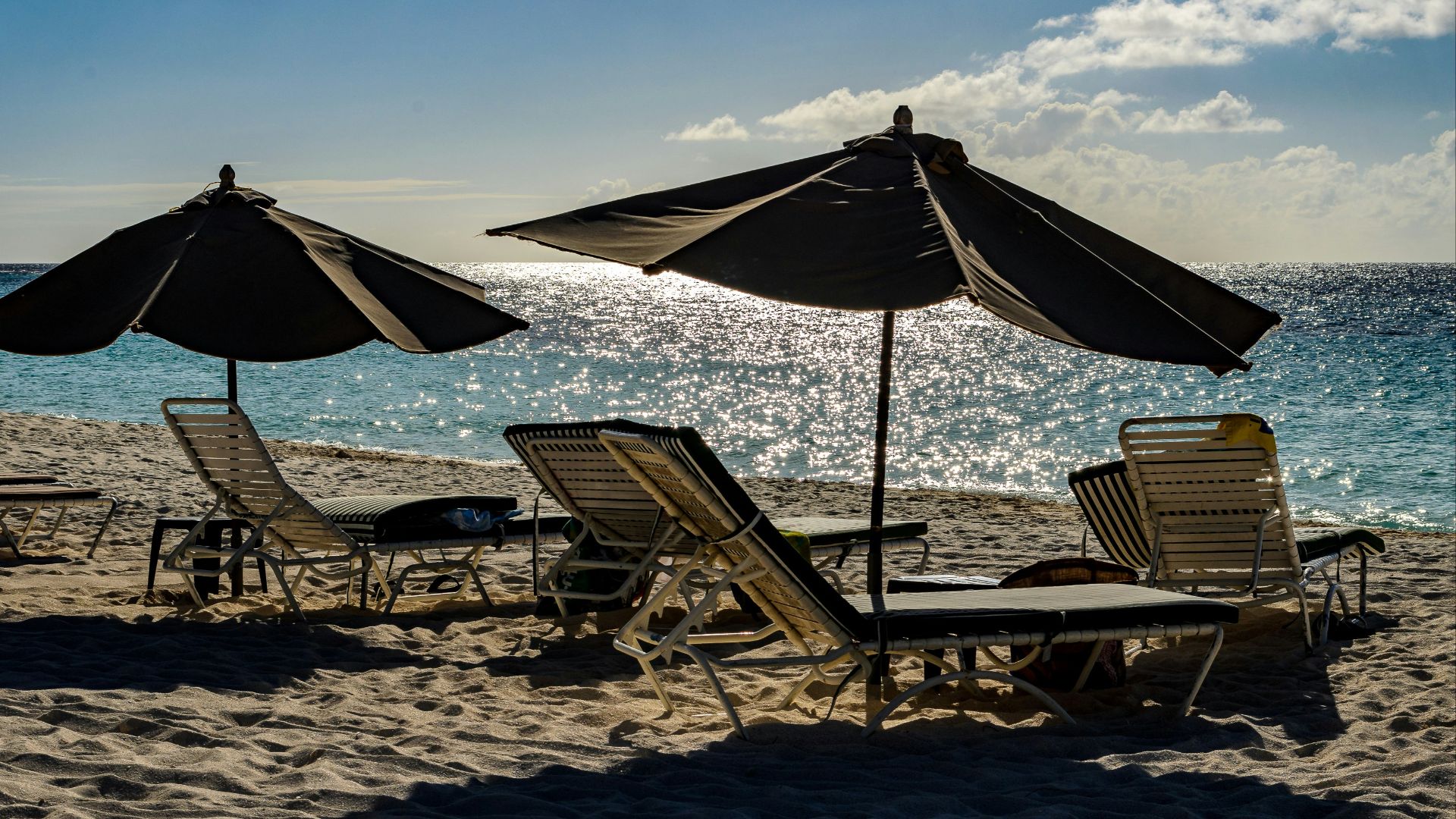 a couple of lawn chairs sitting on top of a sandy beach