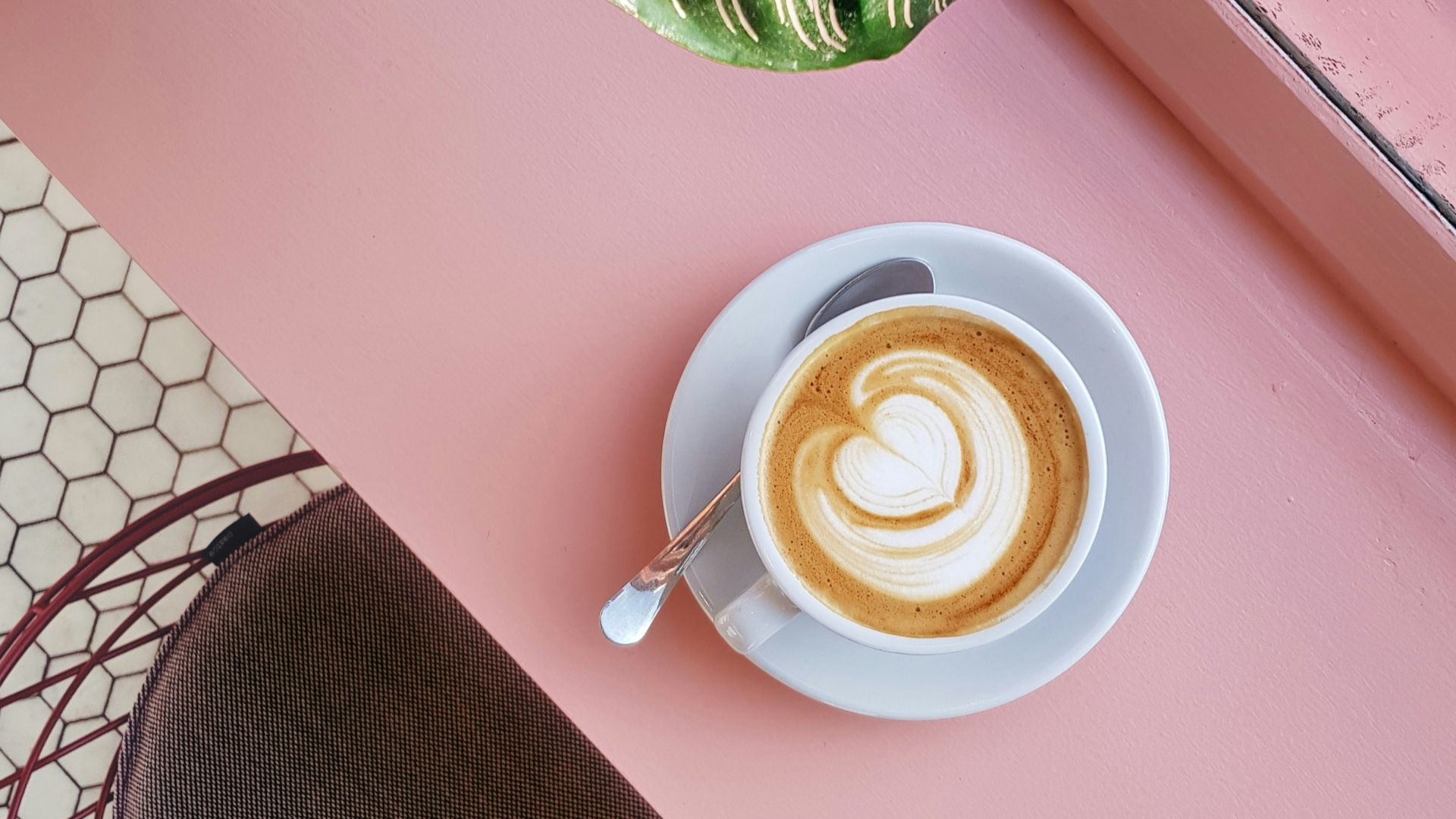 cup of coffee on saucer with teaspoon on pink tabletop