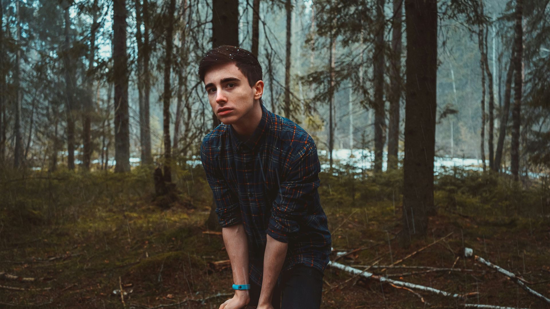 man in black and gray plaid dress shirt and blue denim jeans standing on forest during