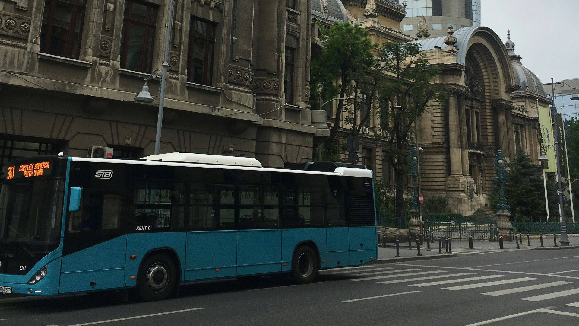a blue bus driving down a street next to a tall building