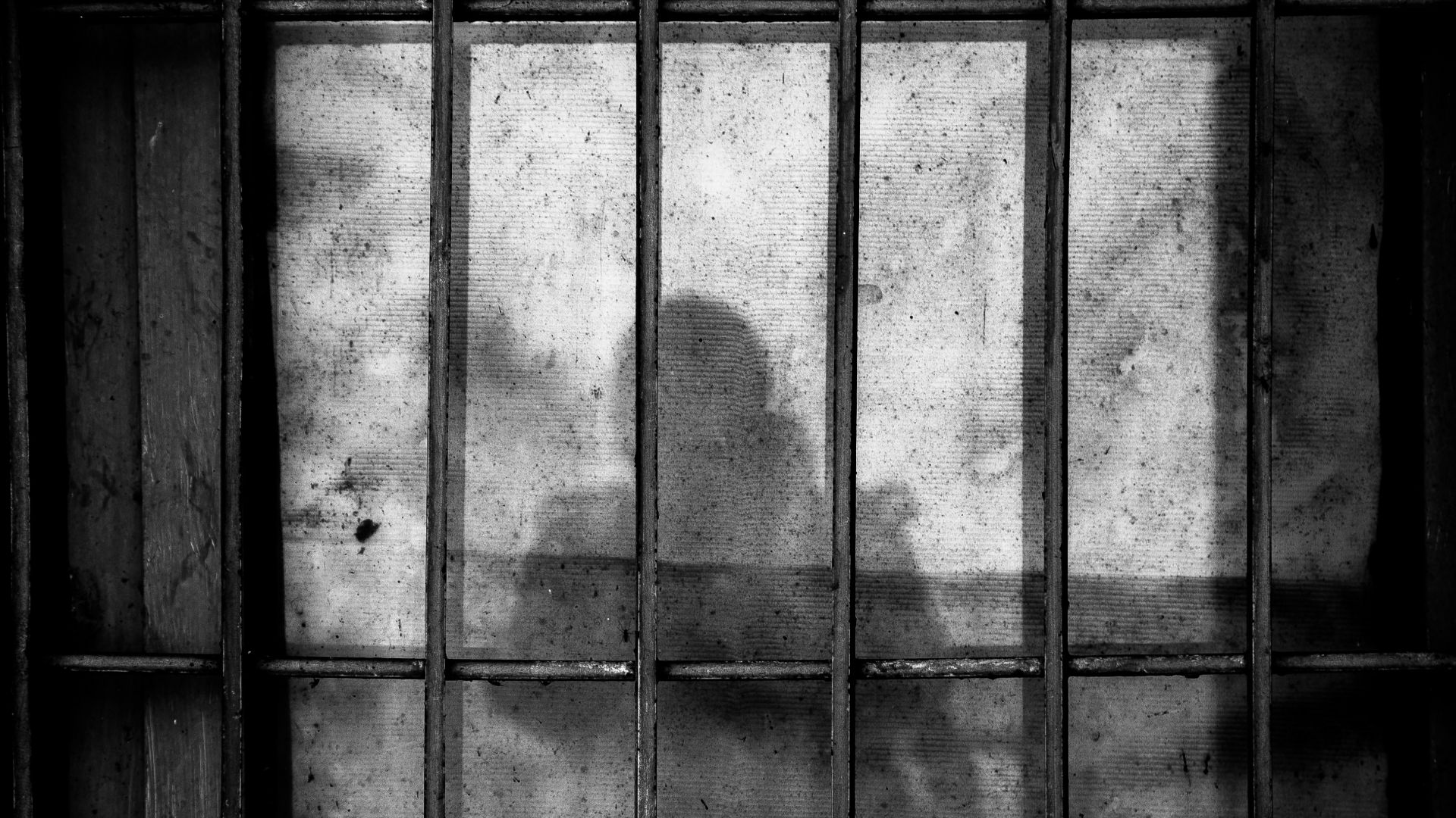 a shadow of a person behind bars in a jail cell
