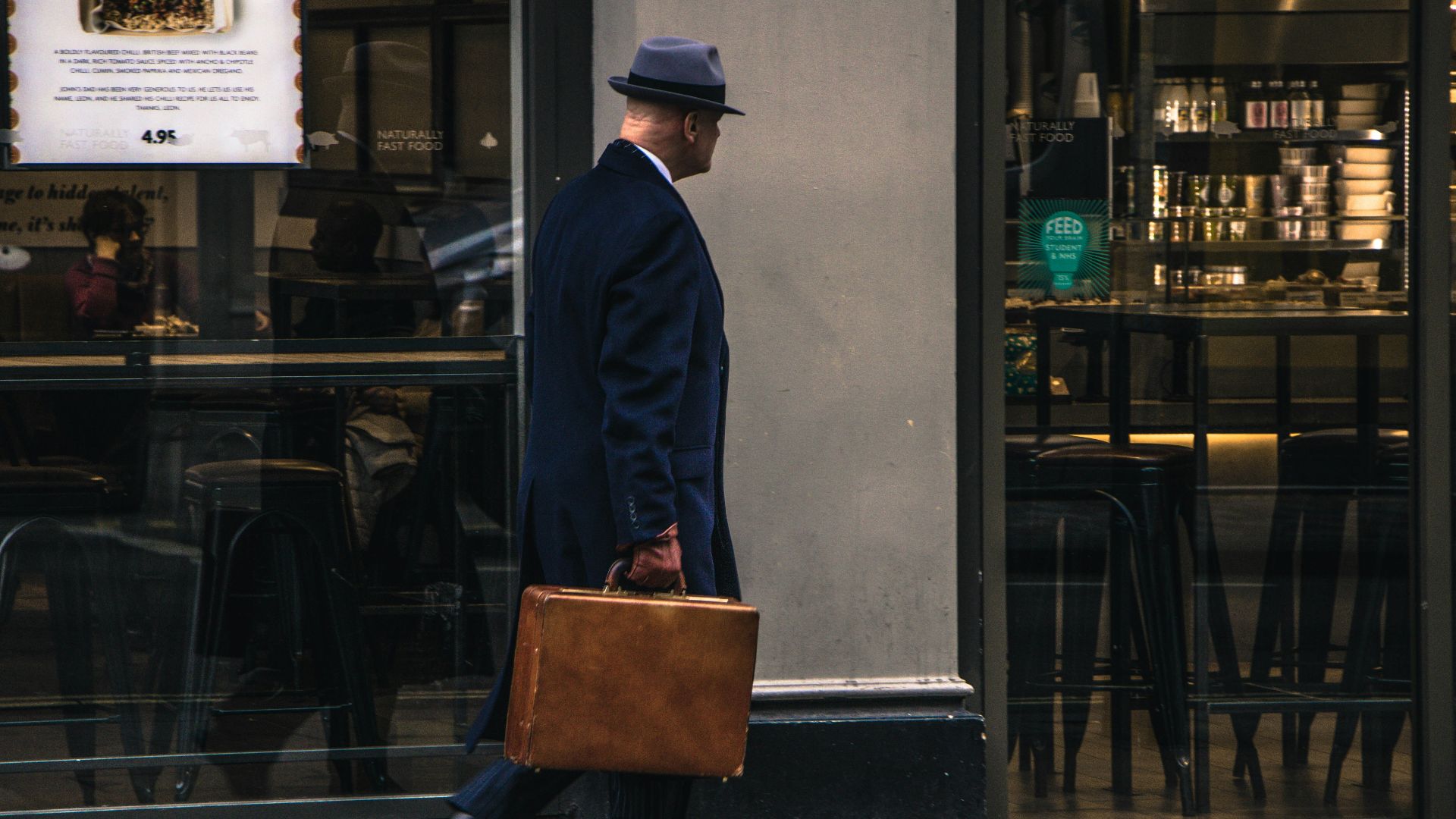 man in black suit jacket and blue hat standing in front of store