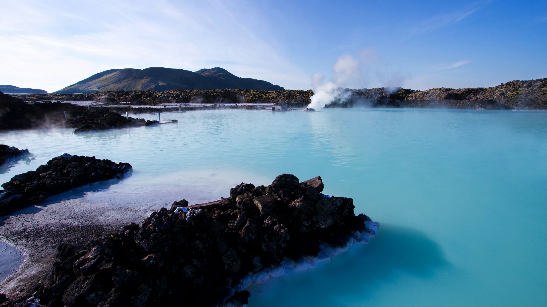 calm water beside mountain under white clouds and blue sky