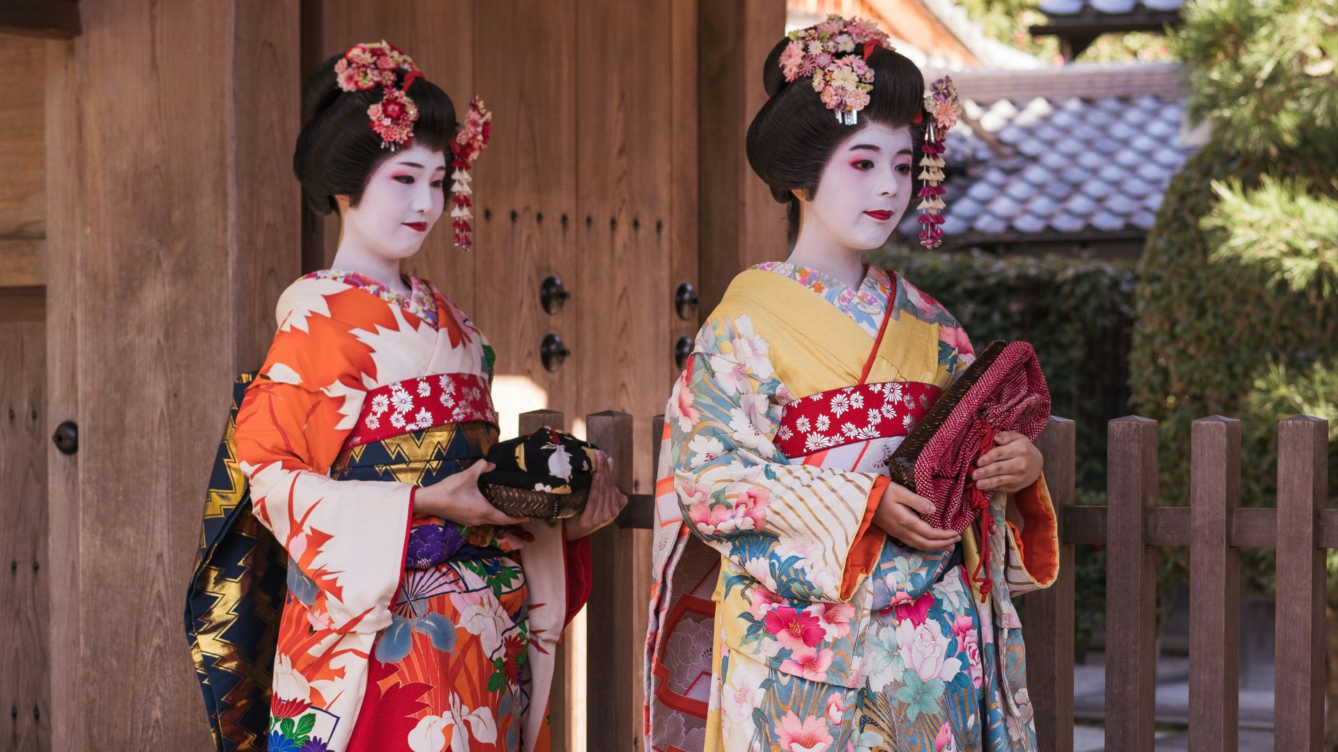 woman in white red and green floral kimono standing beside brown wooden fence during daytime