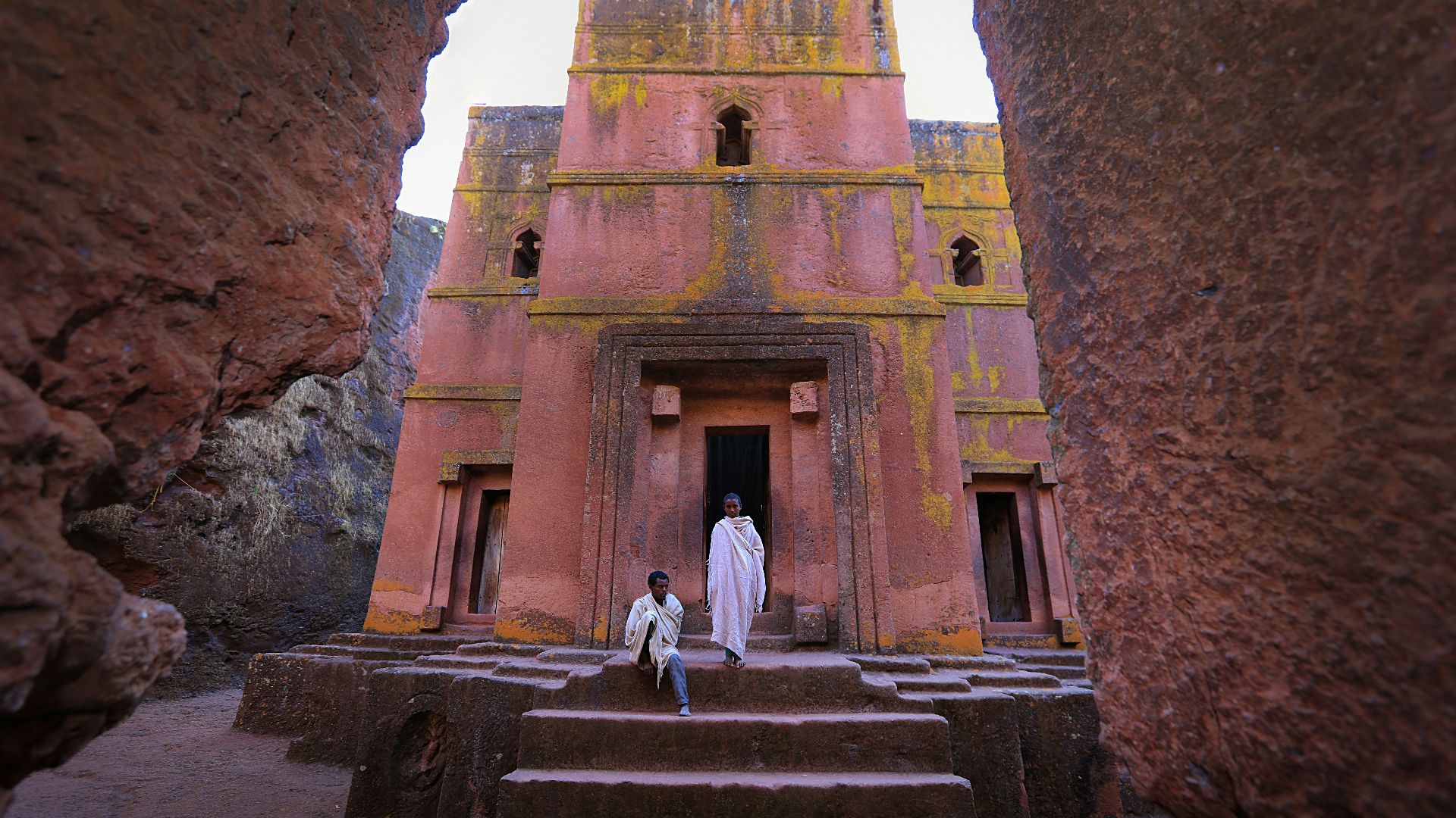 person in white dress in front of pink building