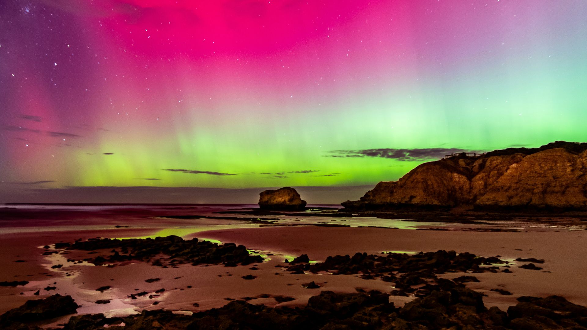 an aurora bore over a rocky beach under a purple sky