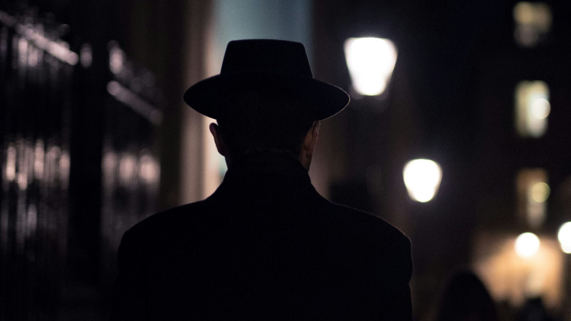 man in black hat walking on sidewalk during night time
