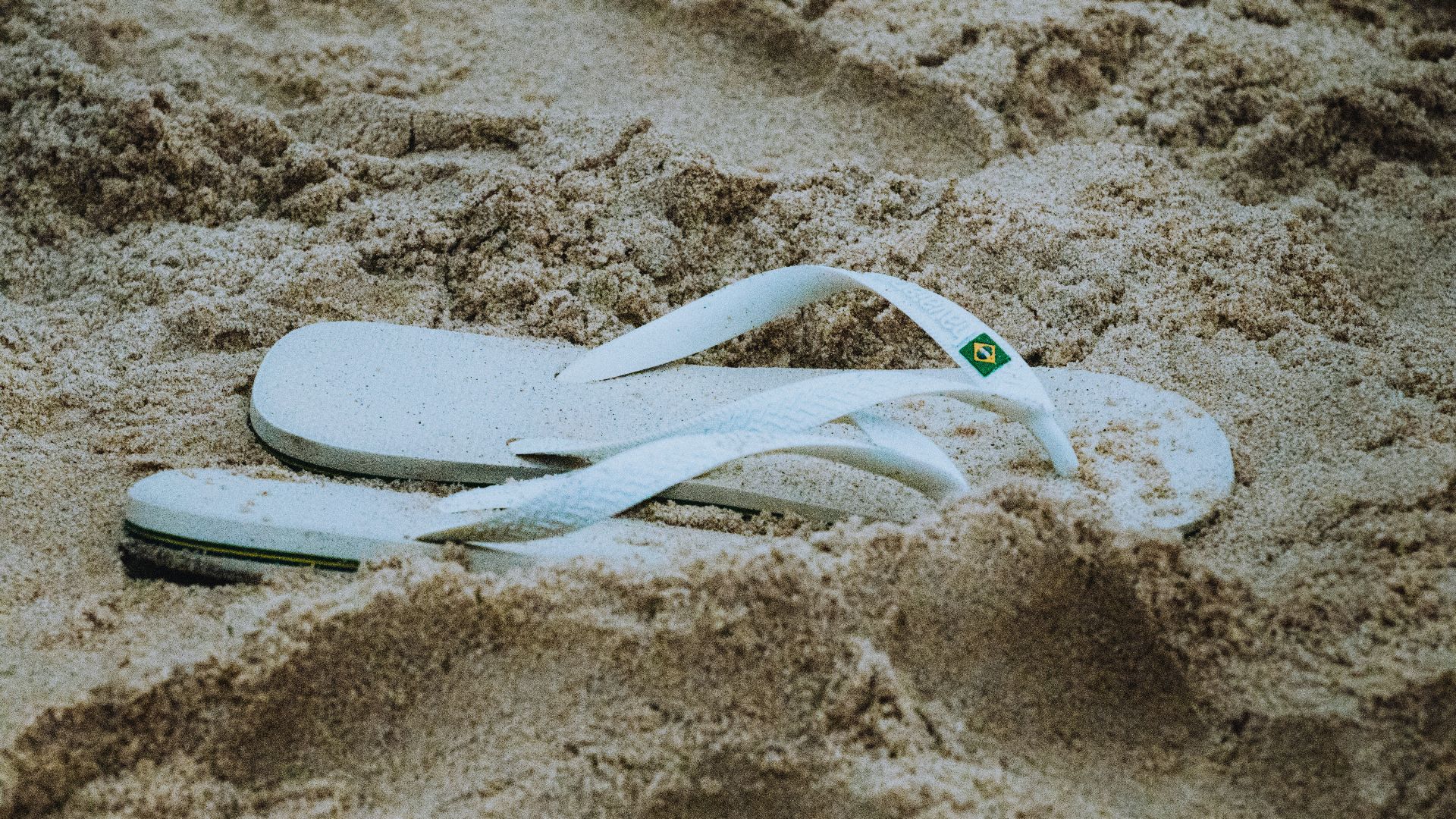 a pair of white flip flops laying in the sand