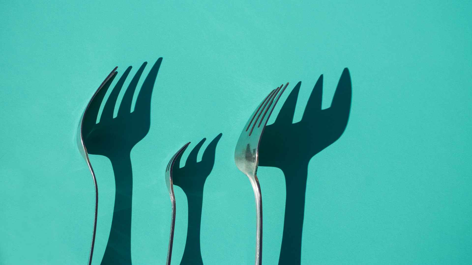 three gray metal forks casting shadow on green surface