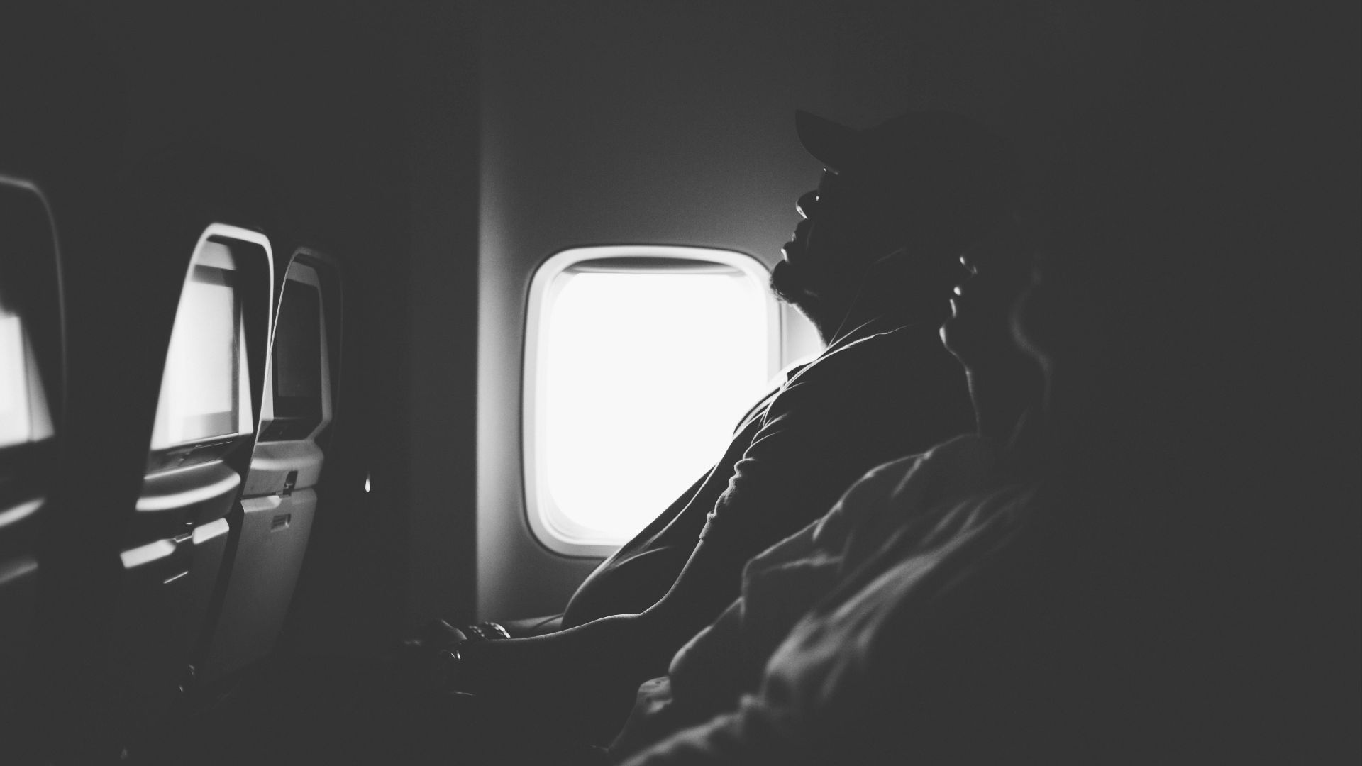 grayscale photo of three person sitting inside airplane