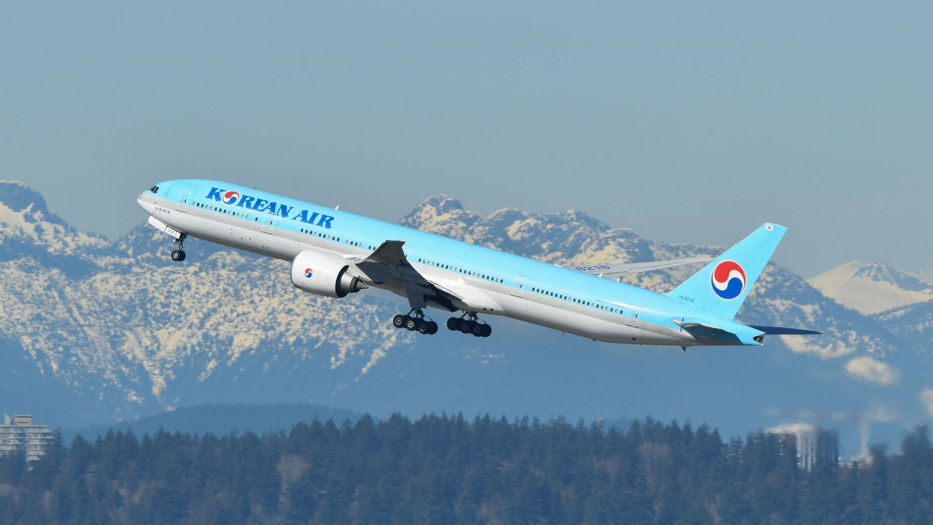 A blue and white airplane flying over a mountain range