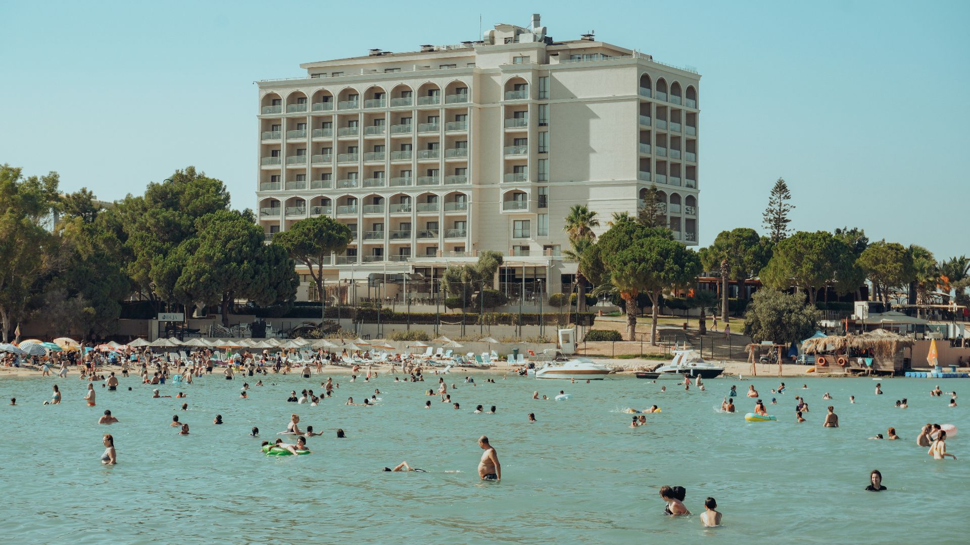 Many people are swimming in the ocean near a hotel