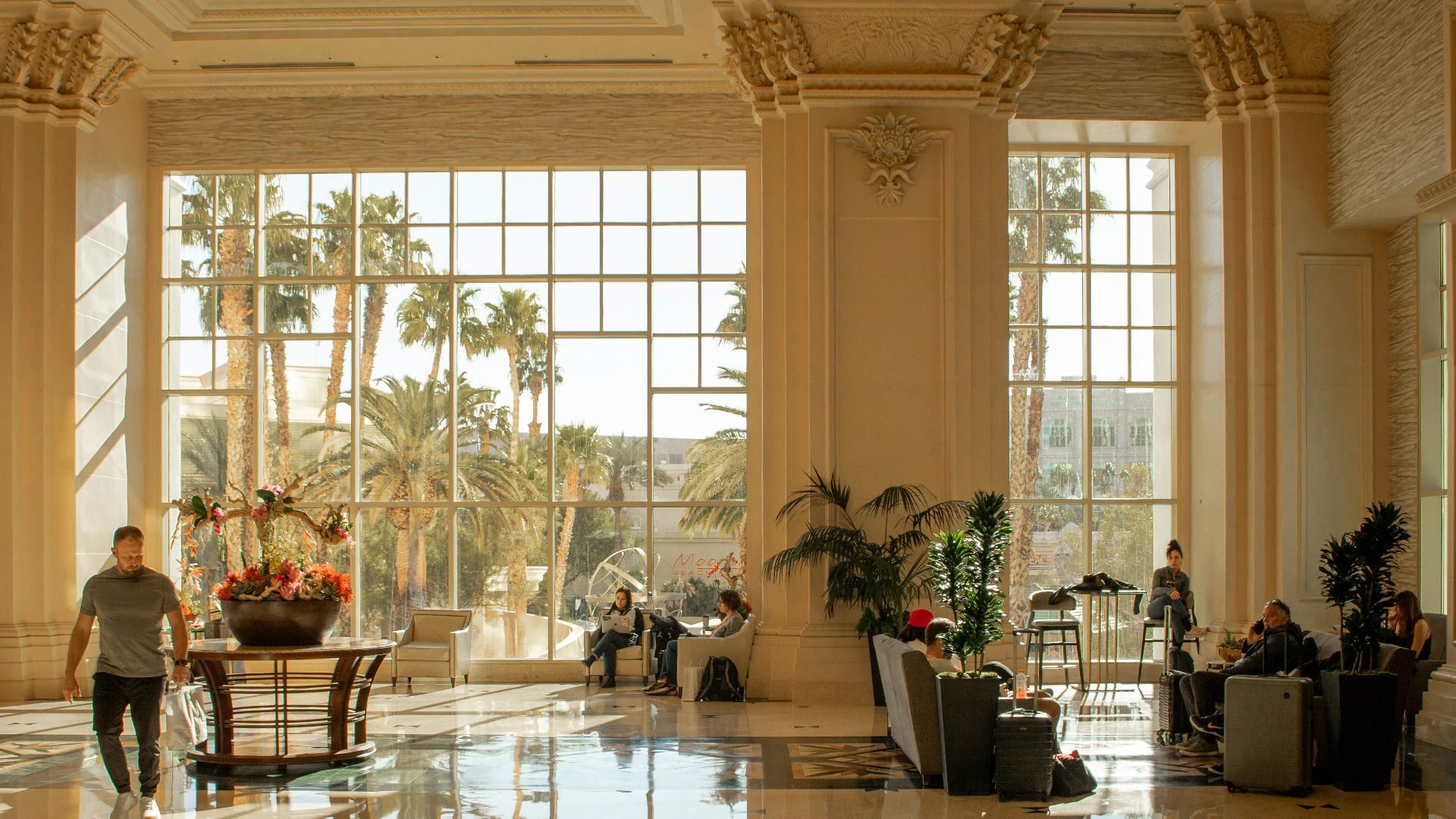 Opulent hotel lobby with sunlight and people relaxing.