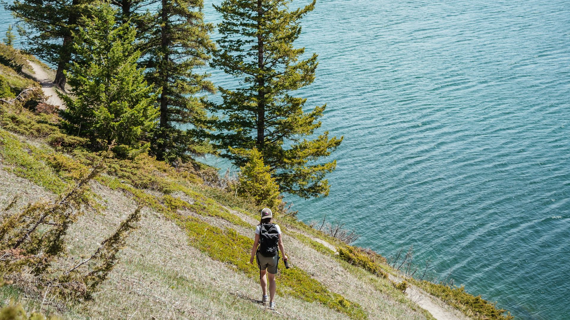 person in black jacket and black pants standing on brown rock near body of water during