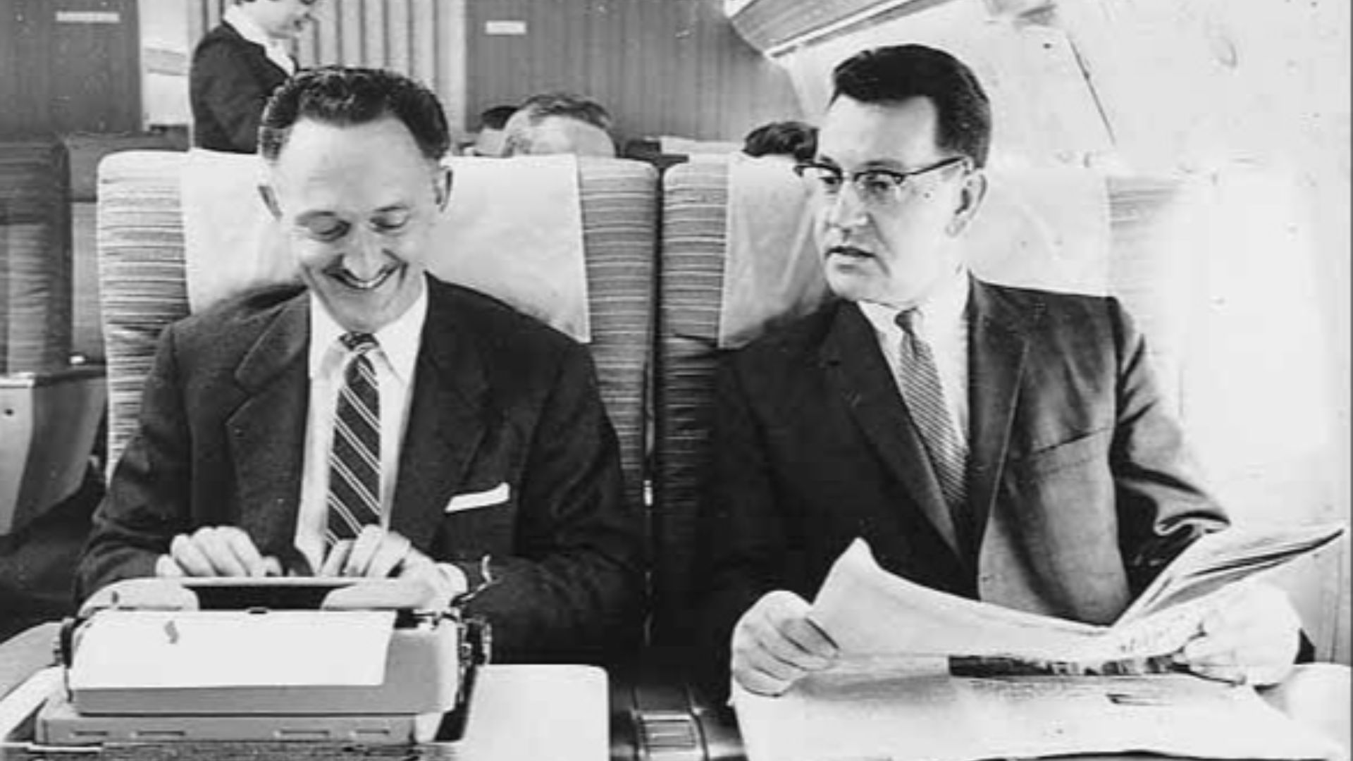 File:Two men on Northwest Airlines aircraft, one using typewriter, with female flight attendant in background (4670206226).jpg
