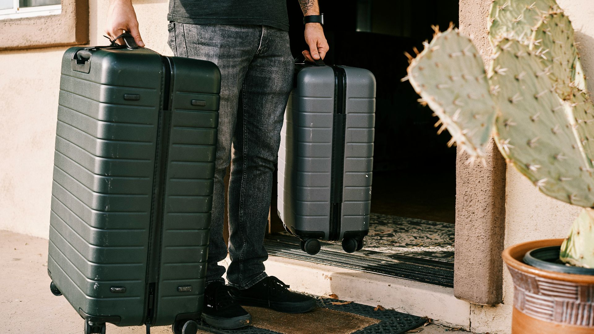 man in black denim jeans and black leather shoes standing beside black luggage bag