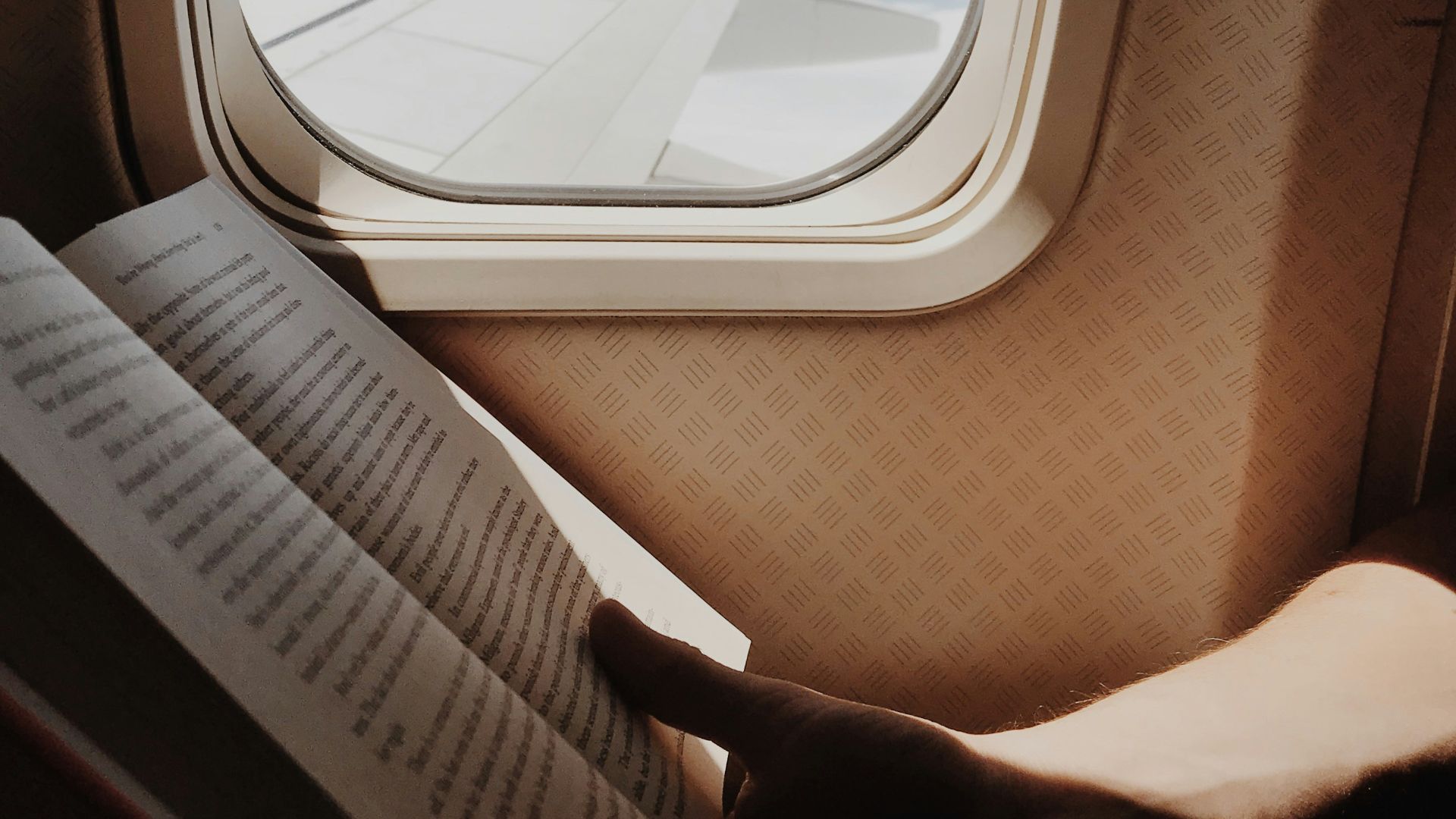 person reading book beside airplane window