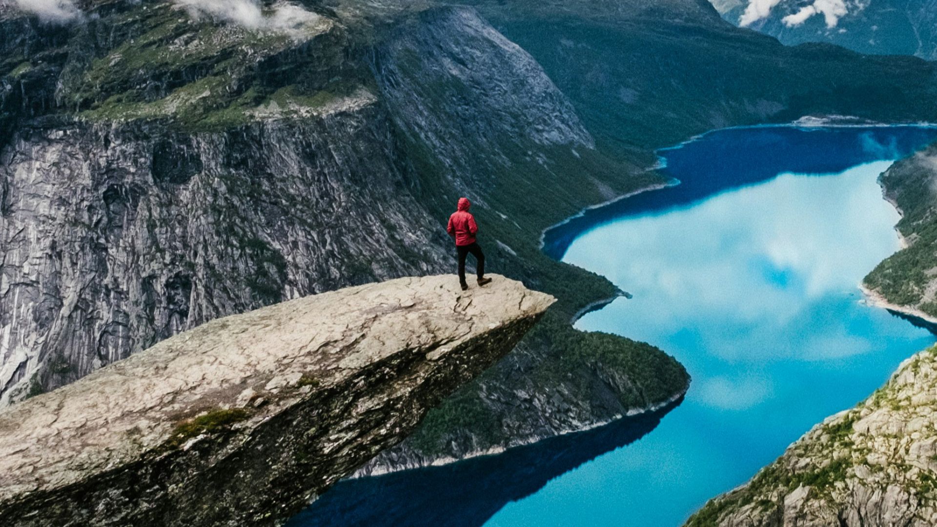 man standing on rock cliff overlooking river near mountain nature photography