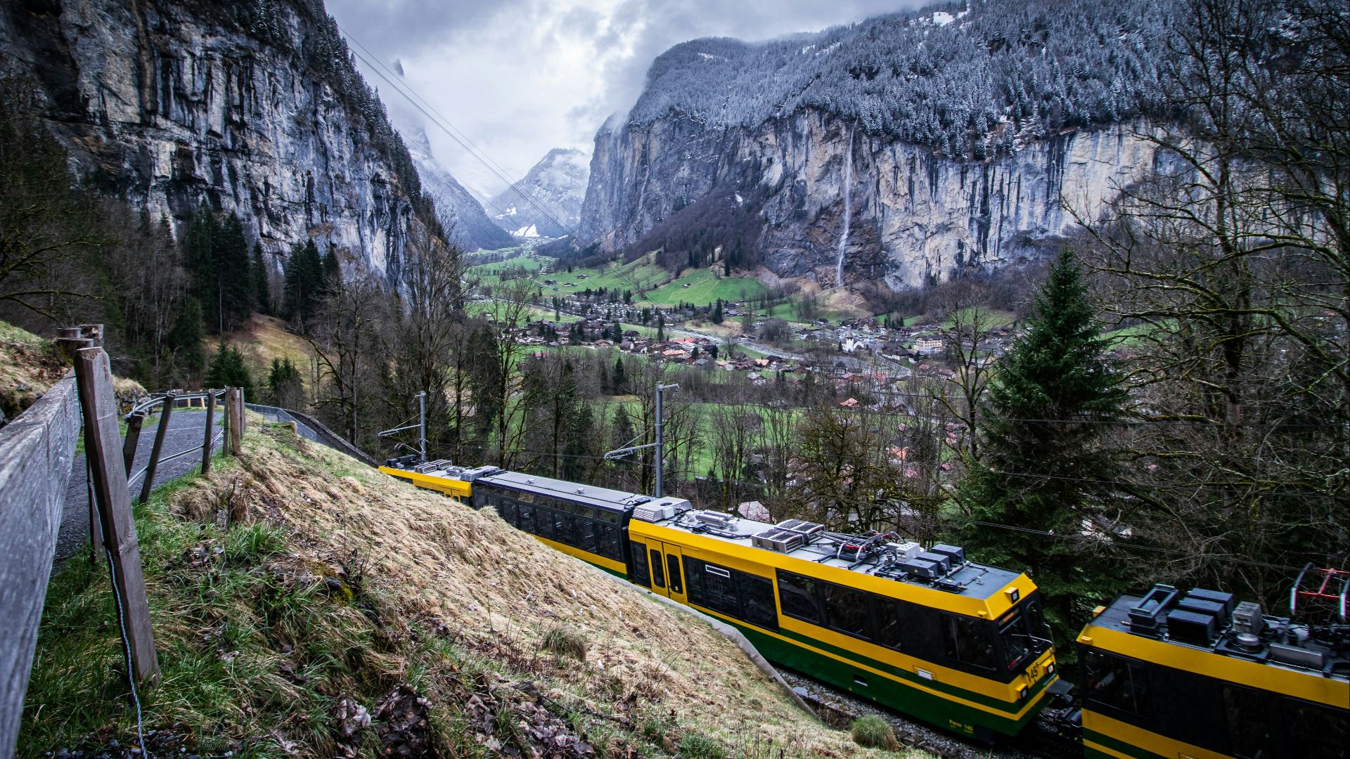 a yellow and black train traveling past a mountain side