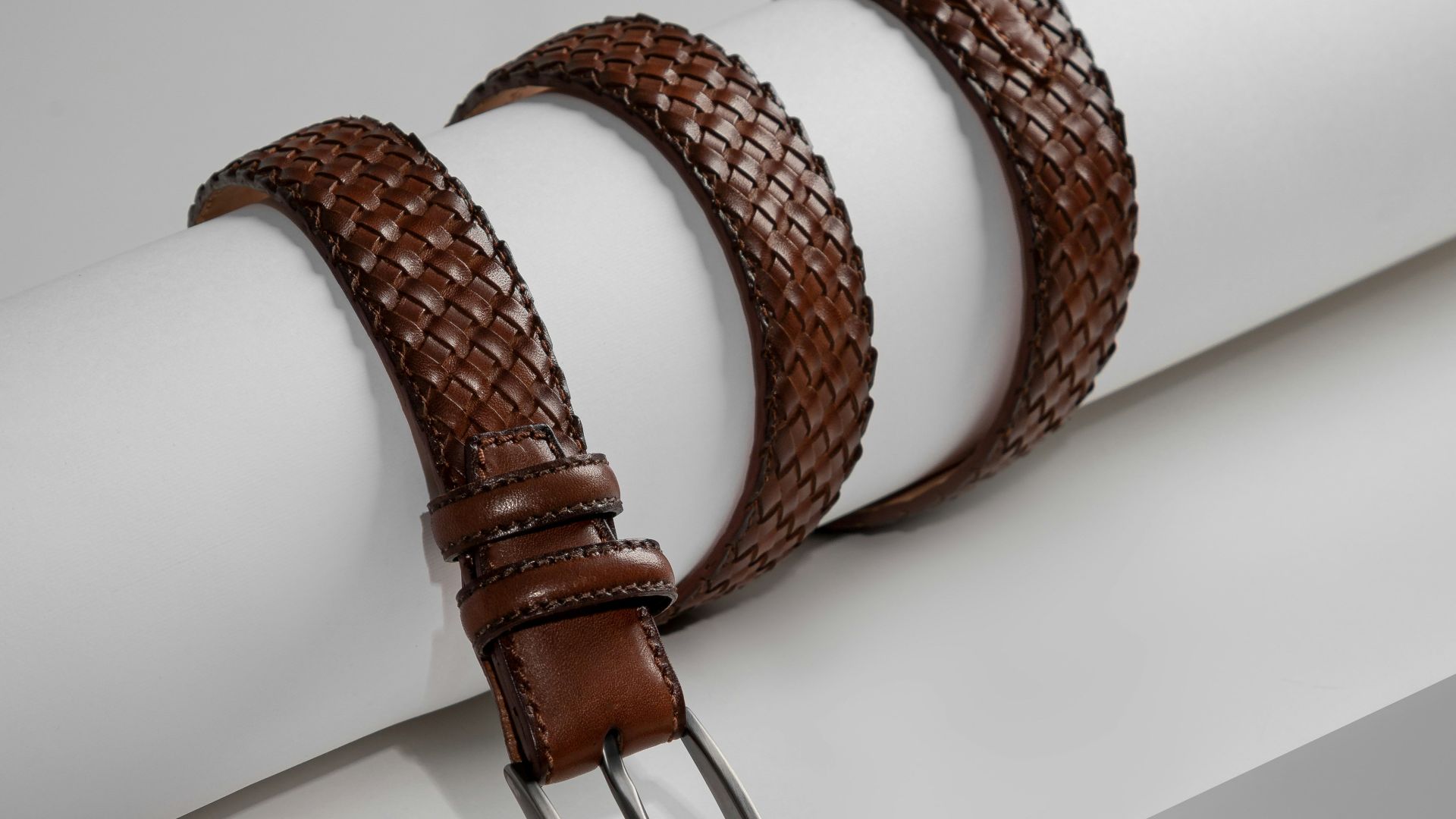 a pair of brown leather belts sitting on top of a white piece of paper