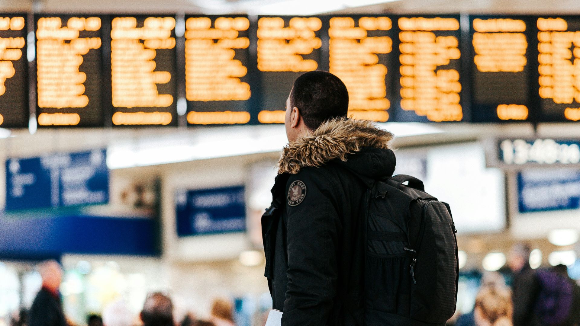 man standing inside airport looking at LED flight schedule bulletin board