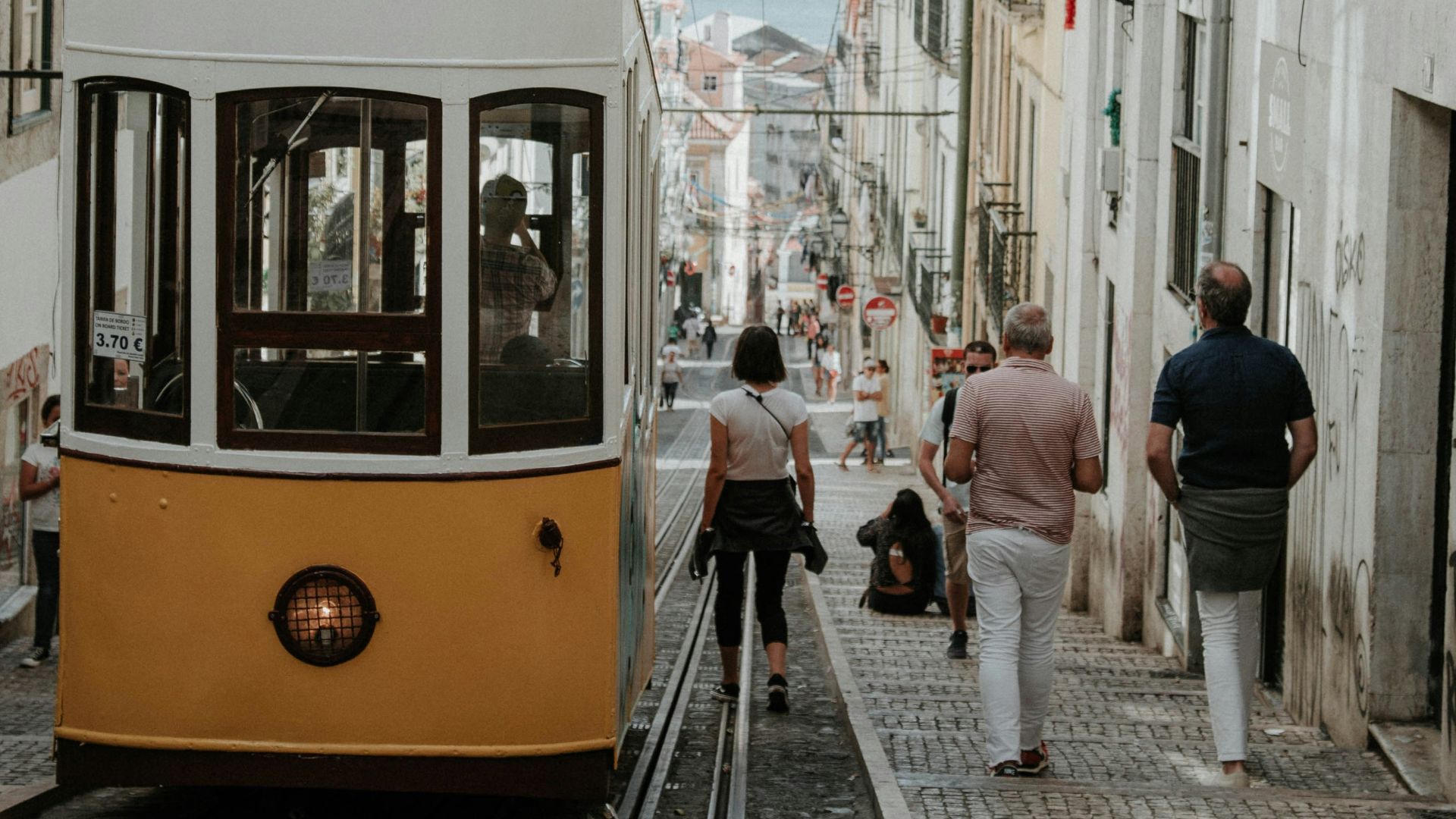 thee person walking near white and orange bus