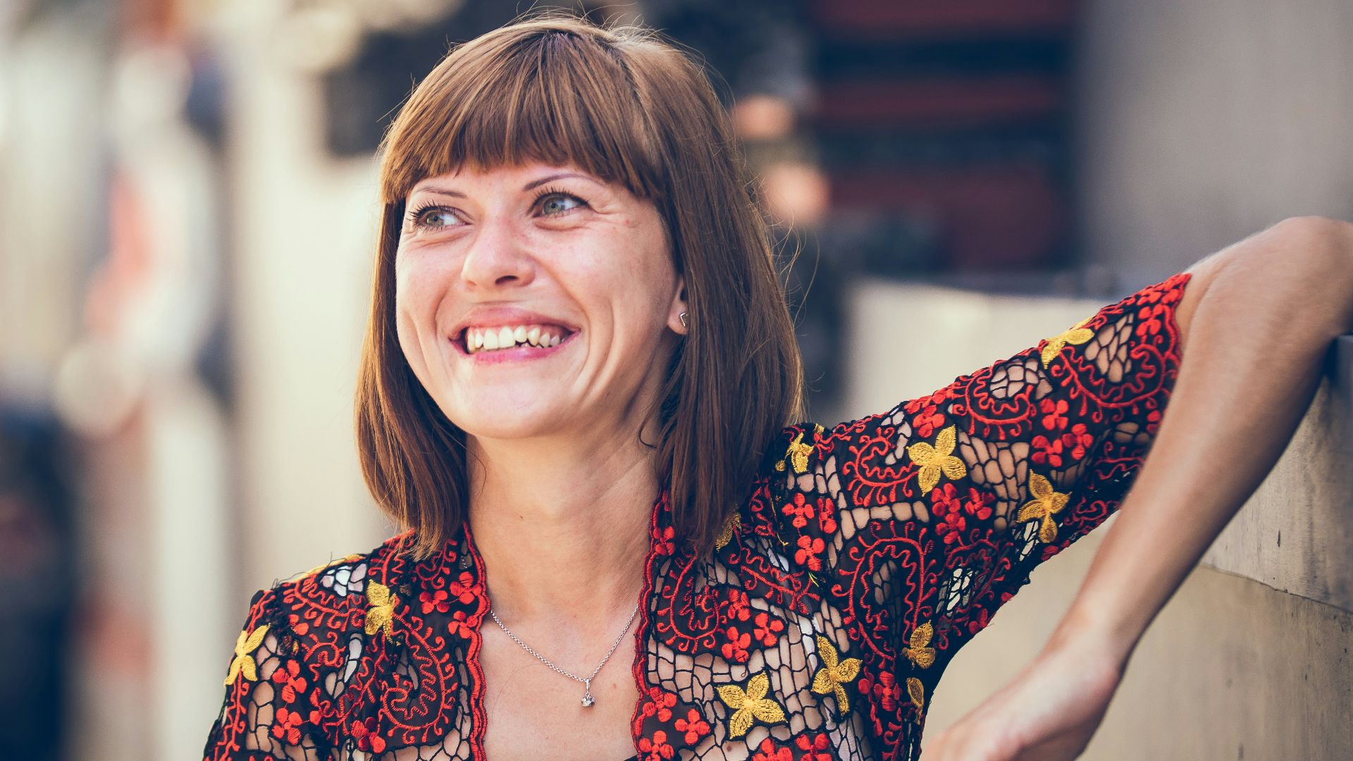 woman in floral-themed cardigan leaning on fence in bokeh photography