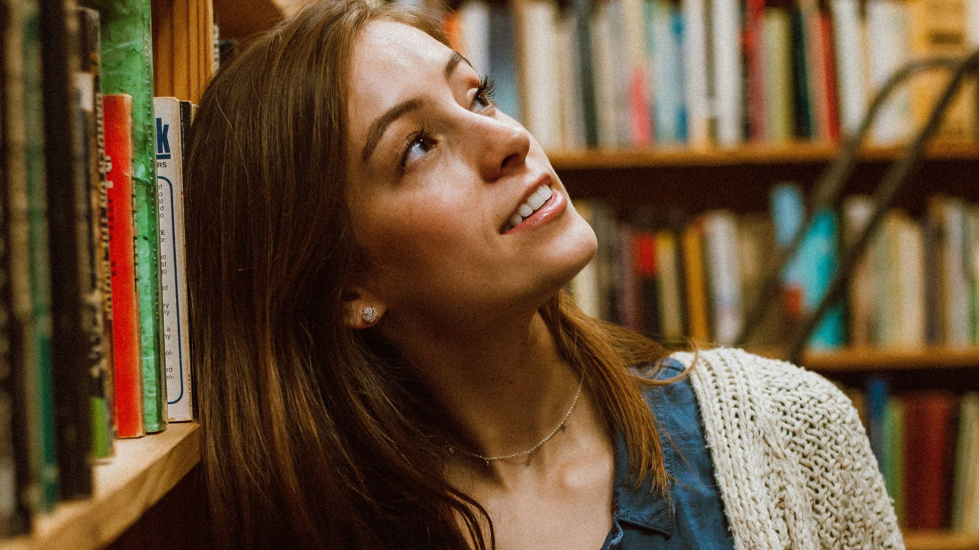 woman in cardigan leaning on bookshelf