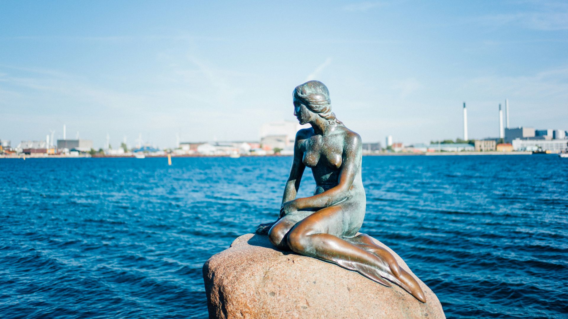 woman sitting on rock statue near body of water during daytime