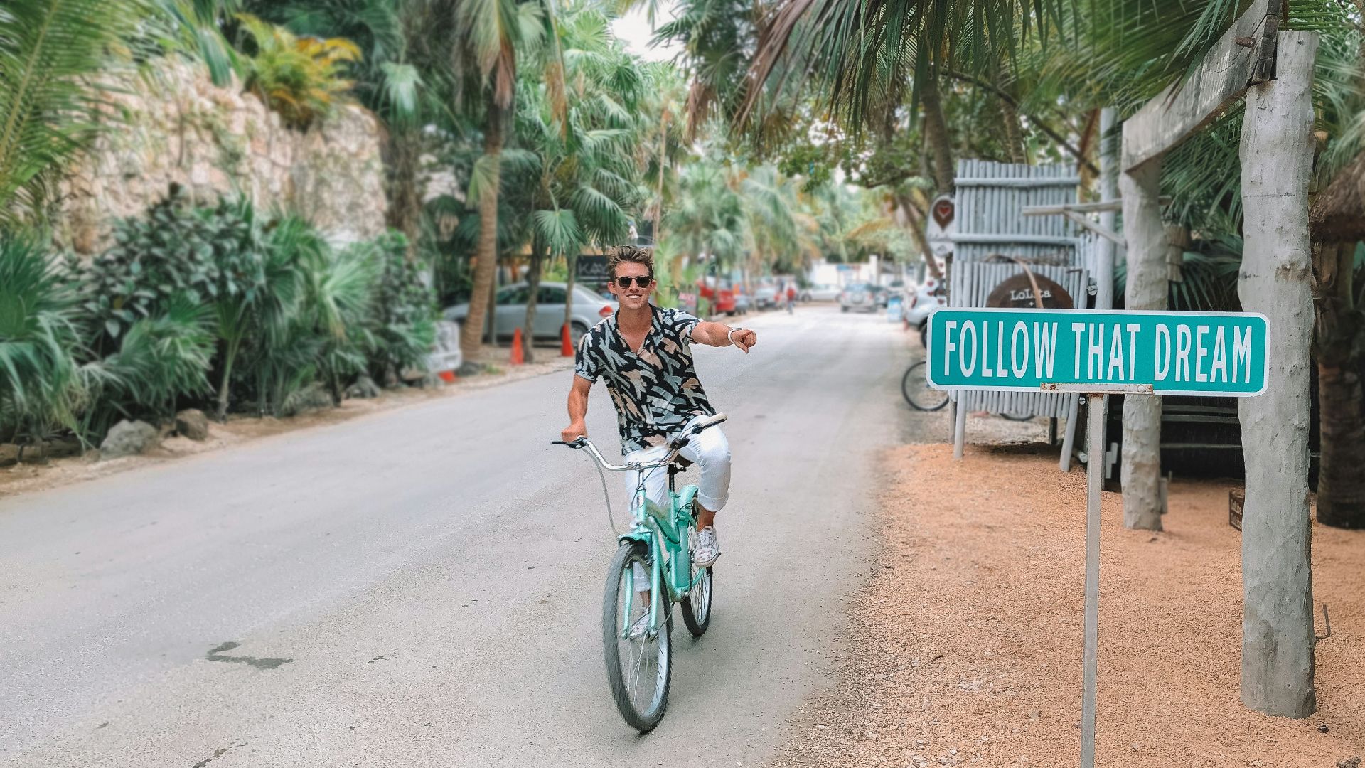 man rides bike pointing to follow that dream signage