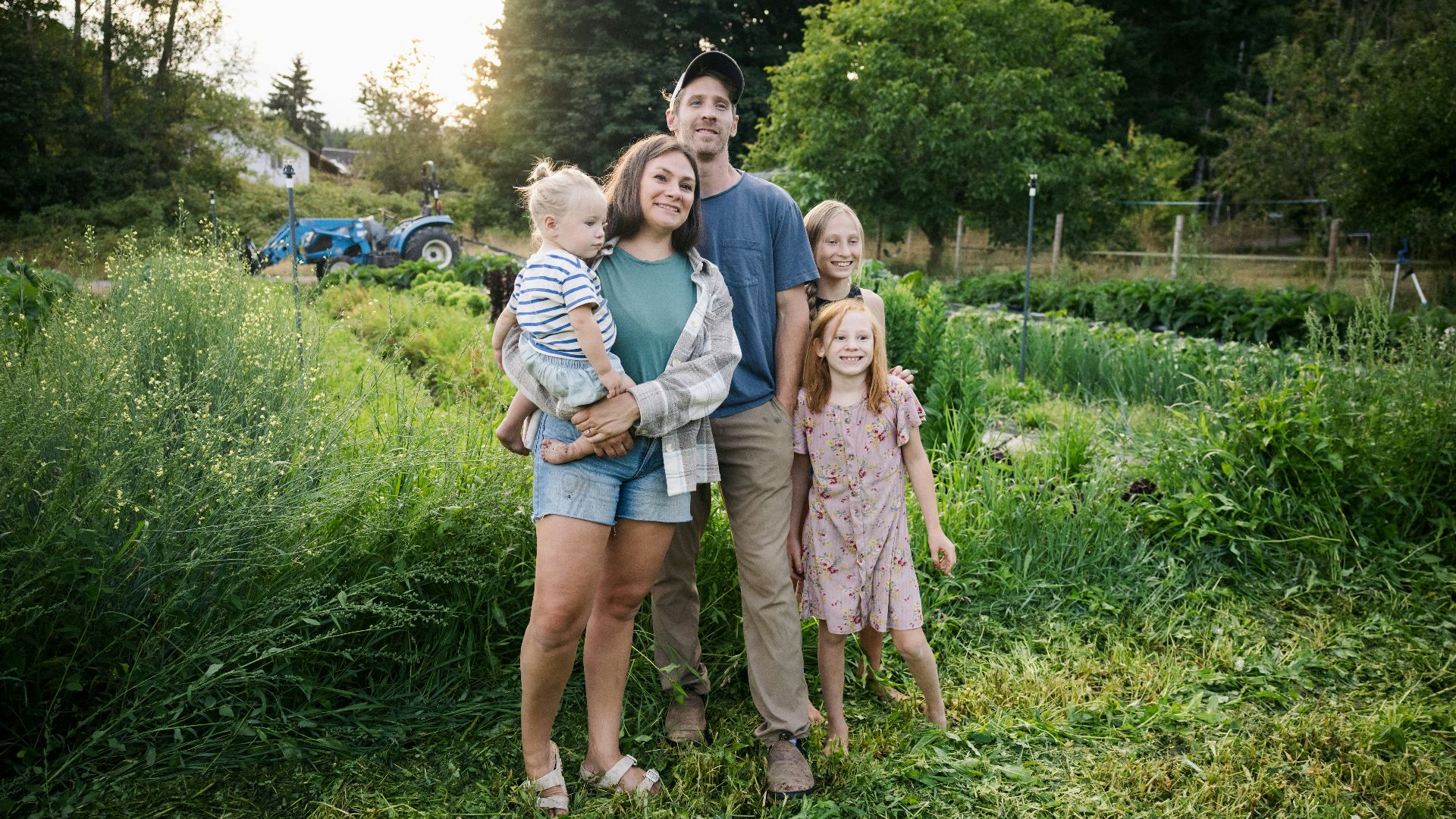 Family standing in a lush green field with tractor.