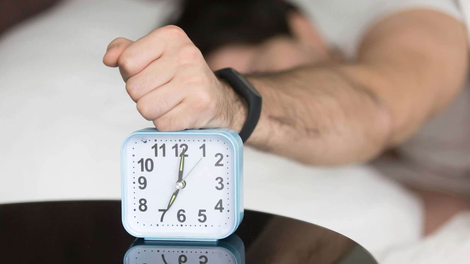 A man laying in bed with a clock on top of him
