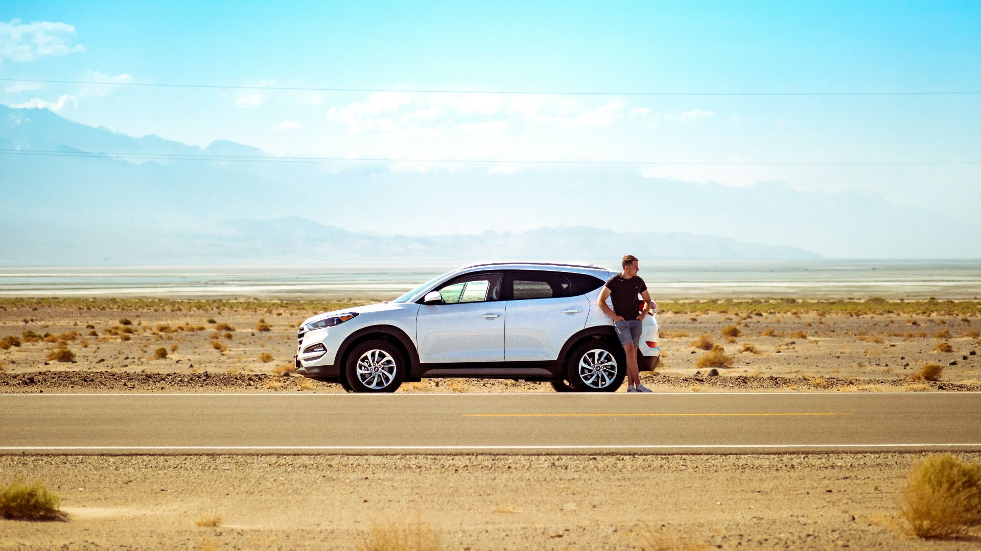 man standing beside white SUV near concrete road under blue sky at daytime
